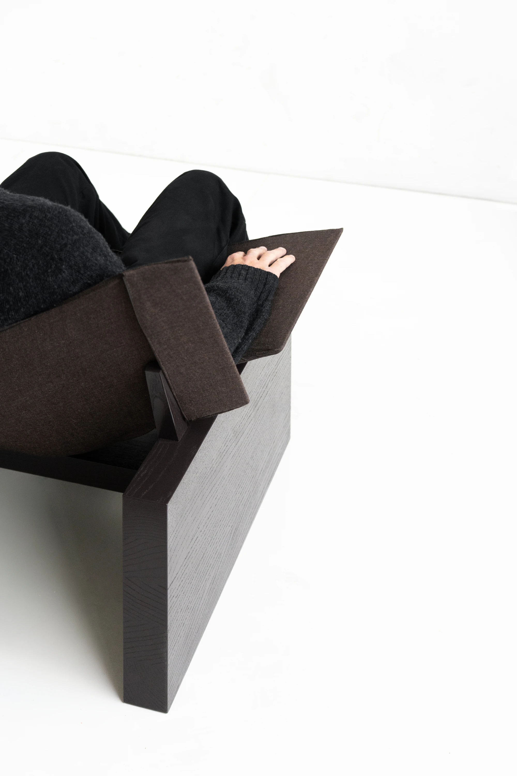 Suspens Lounge Chair by Perron et frères, photographed by Perron et frères — overhead view of a seated figure in dark clothing resting in the chair, hand visible against the wool seat.