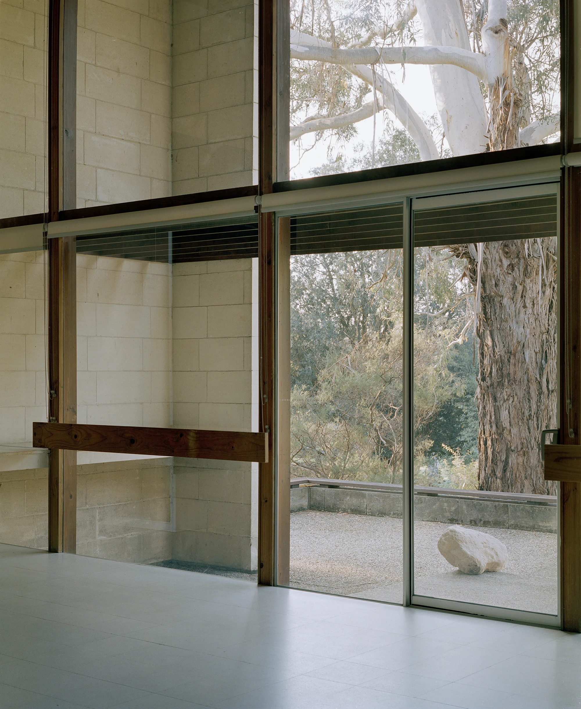 Heide by McGlashan and Everist, photographed by Danny Kai — a gallery interior with limestone block walls, timber framing and a sliding glass door open to a gravel court holding one pale stone.