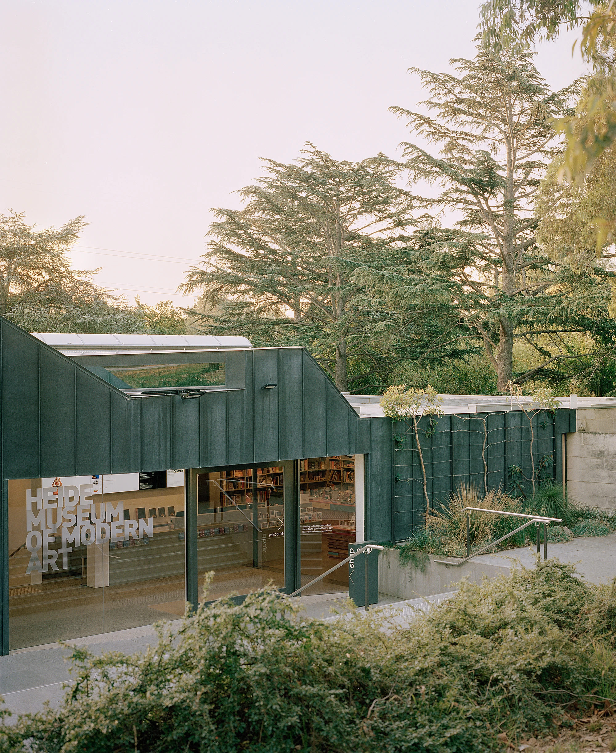 Heide by McGlashan and Everist, photographed by Danny Kai — the dark zinc entry block carries the cut-out HEIDE MUSEUM OF MODERN ART signage above sliding glass and a planted terrace.