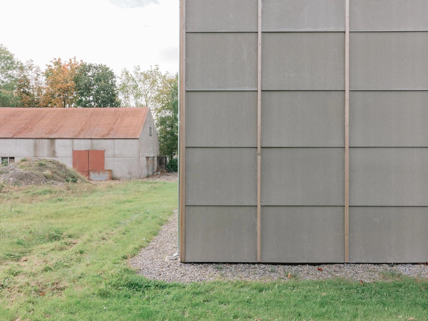 Suburban Family House by O.B. Architect, photographed by Shantanu Starick — the agricultural reference made plain: a corrugated-roofed neighbouring shed across the field beside the panelled gable.