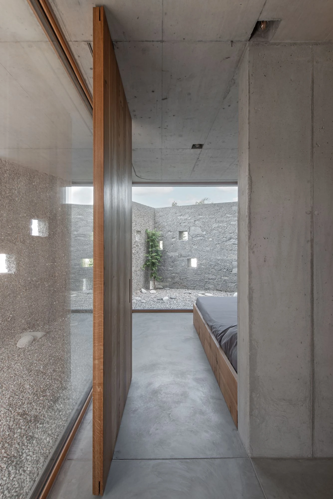 New House in San Nazzaro by Wespi de Meuron Romeo, photographed by Giacomo Albo — a bedroom with oak pivot door opening onto its private courtyard.