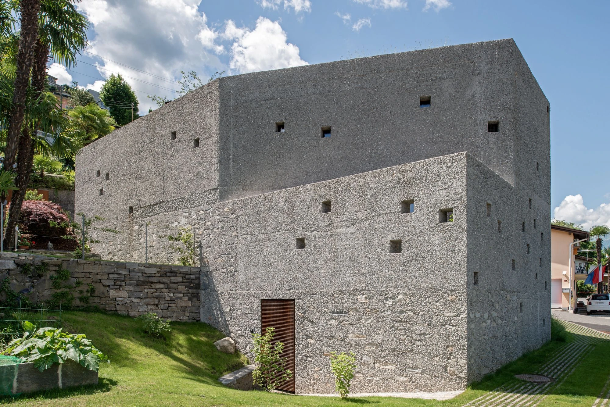 New House in San Nazzaro by Wespi de Meuron Romeo, photographed by Giacomo Albo — the washed-concrete volume seen from the valley side at daytime, with Lago Maggiore and the Ticinese mountains beyond.