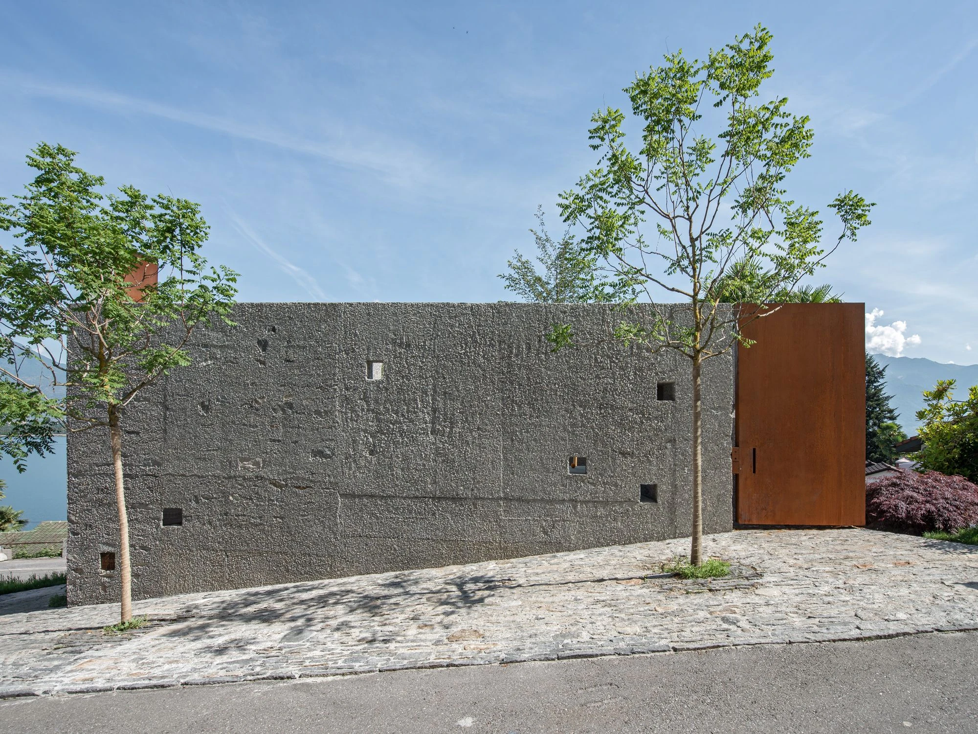 New House in San Nazzaro by Wespi de Meuron Romeo, photographed by Giacomo Albo — natural stone paving and trees forming the three-metre forecourt to the street.