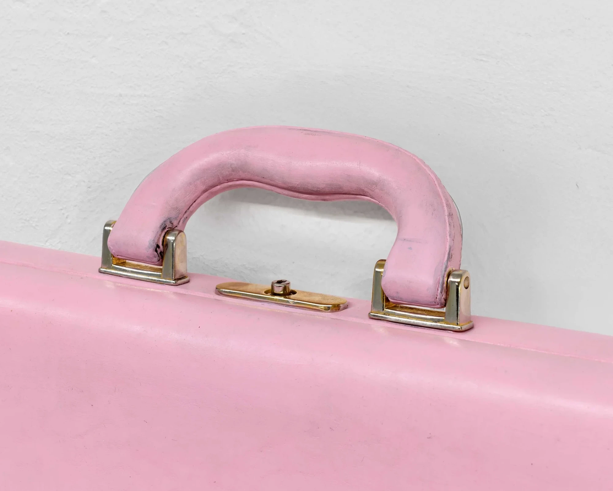 Macro detail of the pink briefcase's padded handle and brass lock catch, the leather rubbed to a velvety finish across the grip.