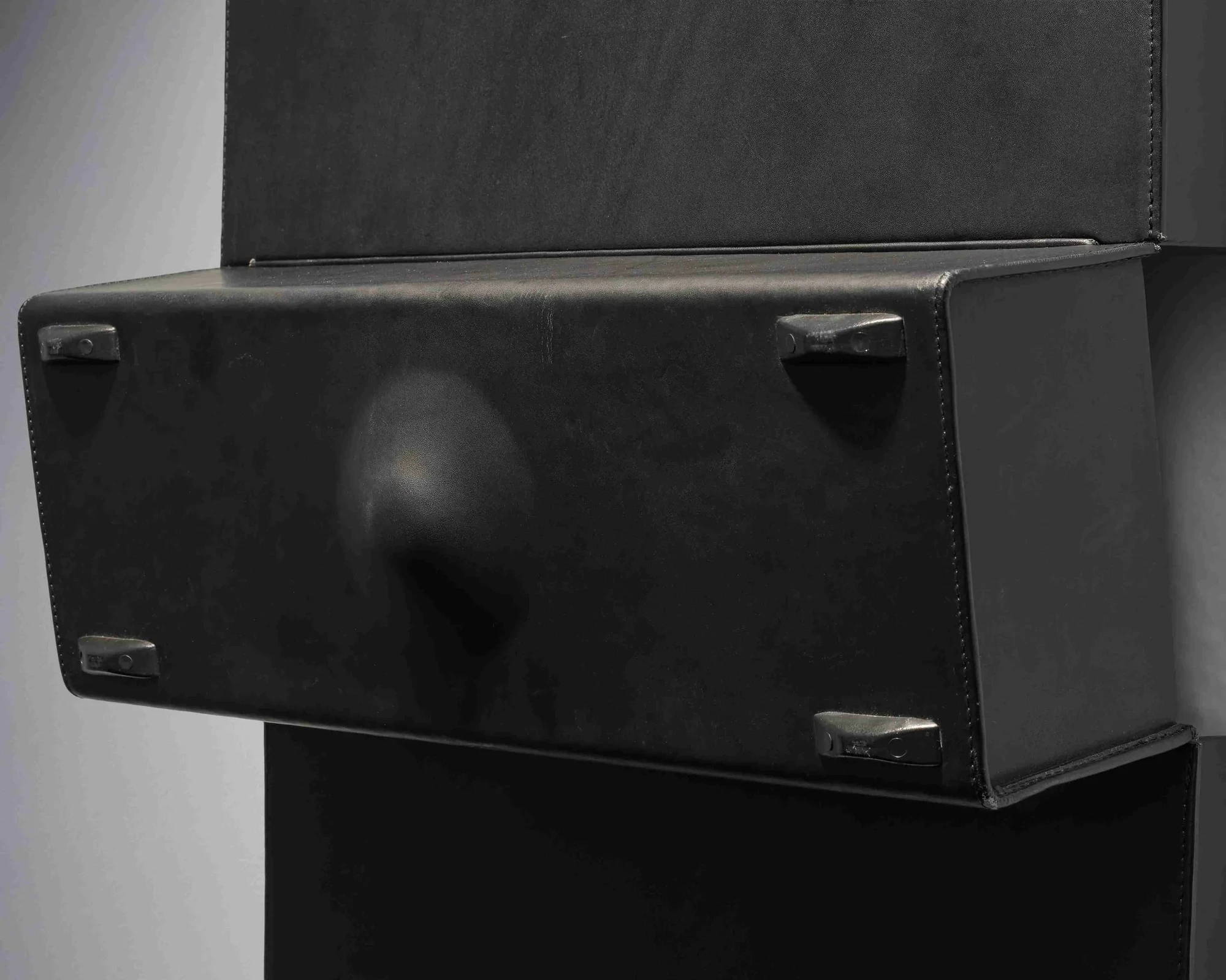 Detail of the middle section of an opened black briefcase sculpture, a soft rounded form pushing from inside the leather shell.