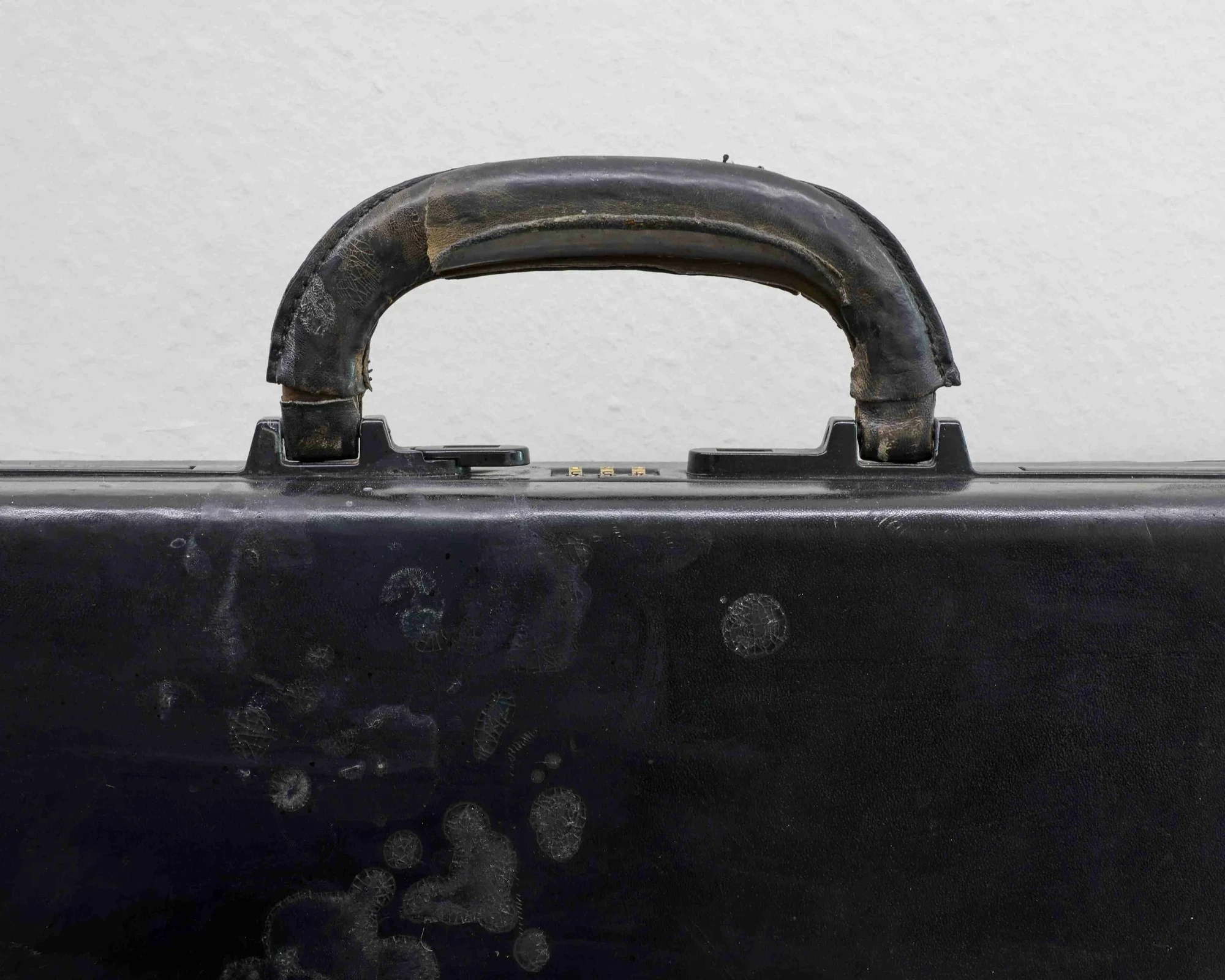 Close-up of a black briefcase handle showing brass lock studs and pale crystalline residue trailing down the case's top edge.