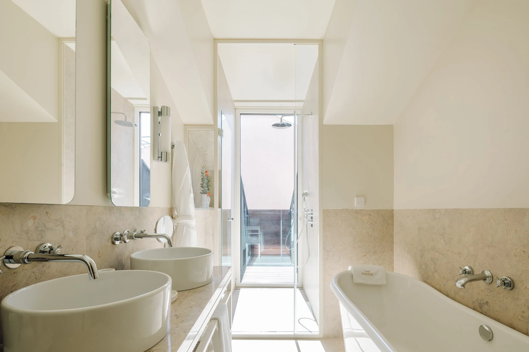 The Ivens by Lázaro Rosa-Violan, photographed by Francisco Nogueira — twin-basin bathroom with travertine counter, freestanding tub and terrace-opening shower.