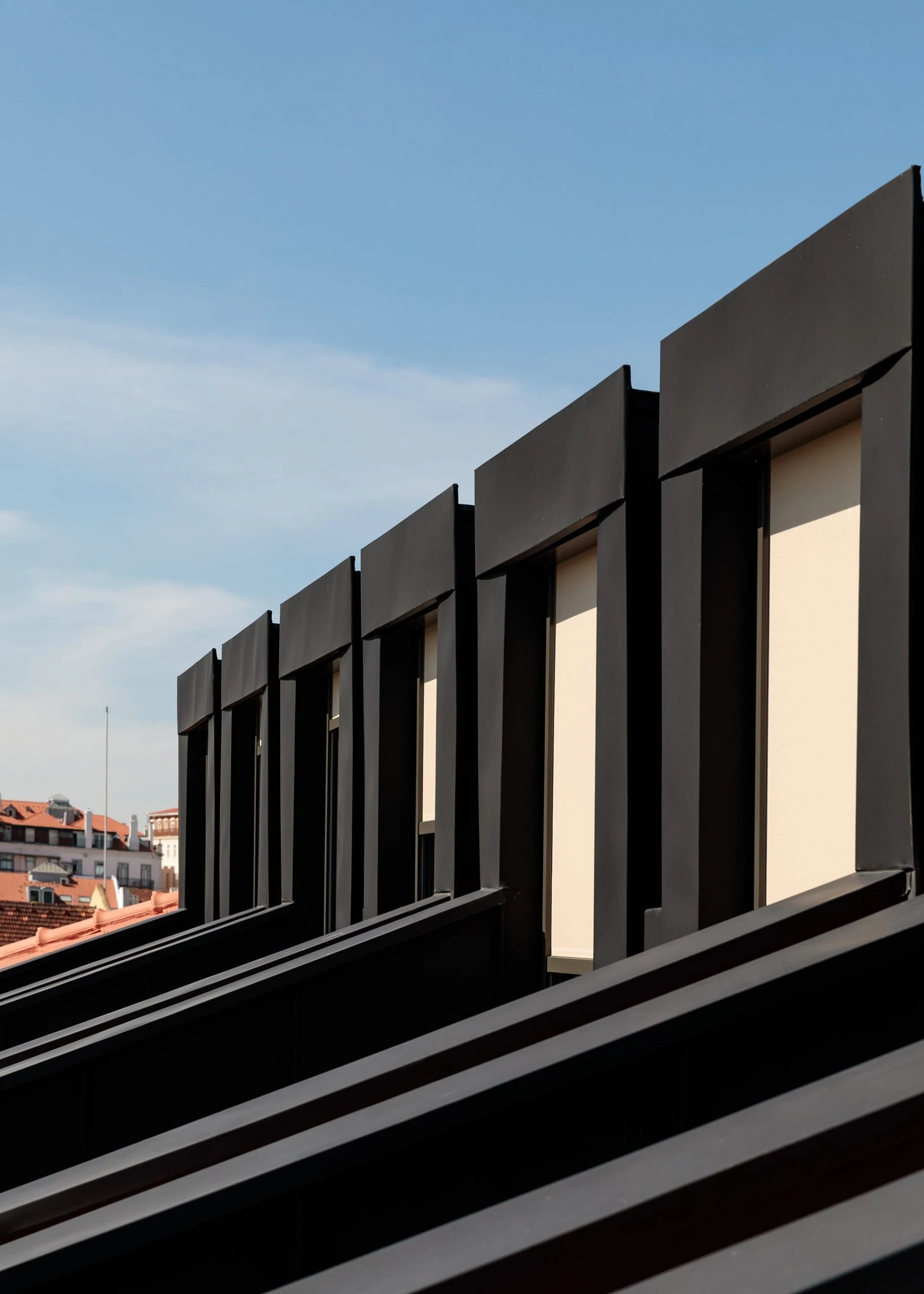 The Ivens by Lázaro Rosa-Violan, photographed by Francisco Nogueira — black mansard dormers stepping along the roofline against Lisbon terracotta and sky.