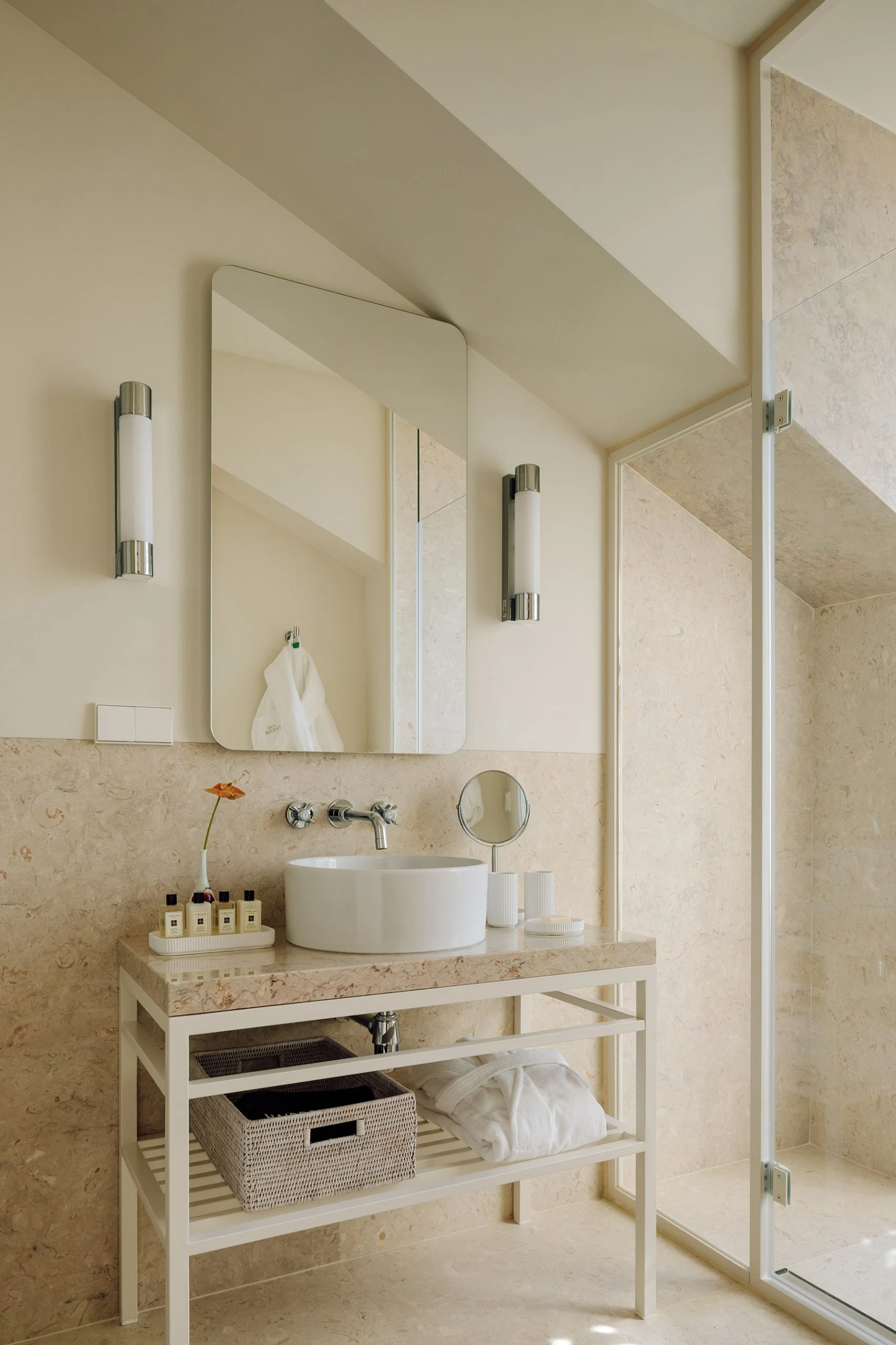 The Ivens by Lázaro Rosa-Violan, photographed by Francisco Nogueira — bathroom with pale travertine vanity, round porcelain basin and polished chrome sconces.
