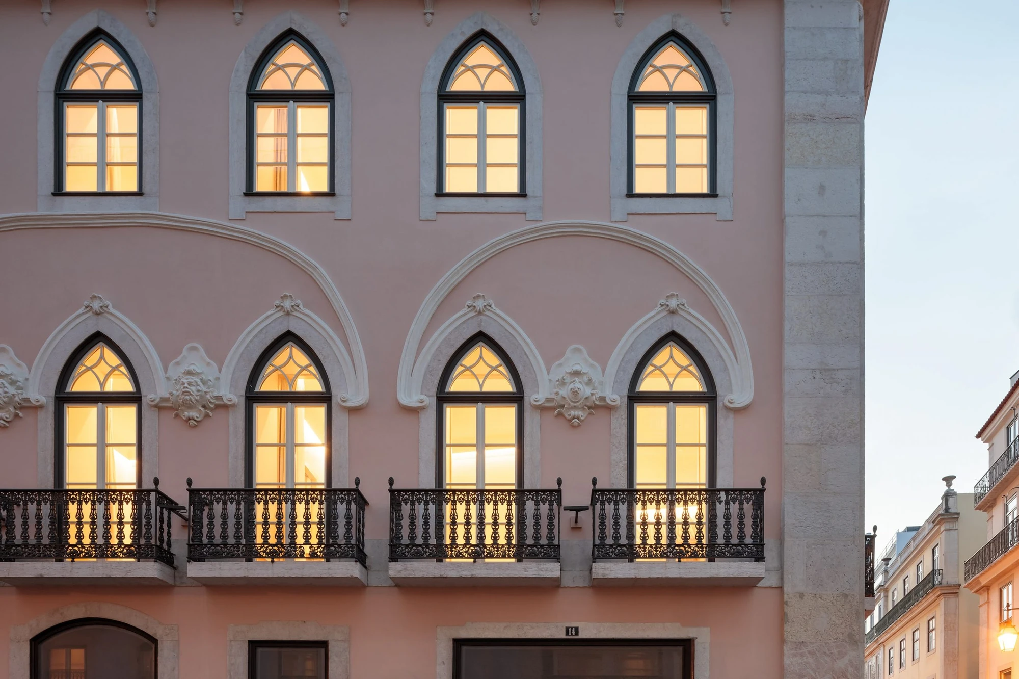 The Ivens by Lázaro Rosa-Violan, photographed by Francisco Nogueira — facade at dusk with lit pointed arch windows, pink stucco and cast-iron filigree balconies.