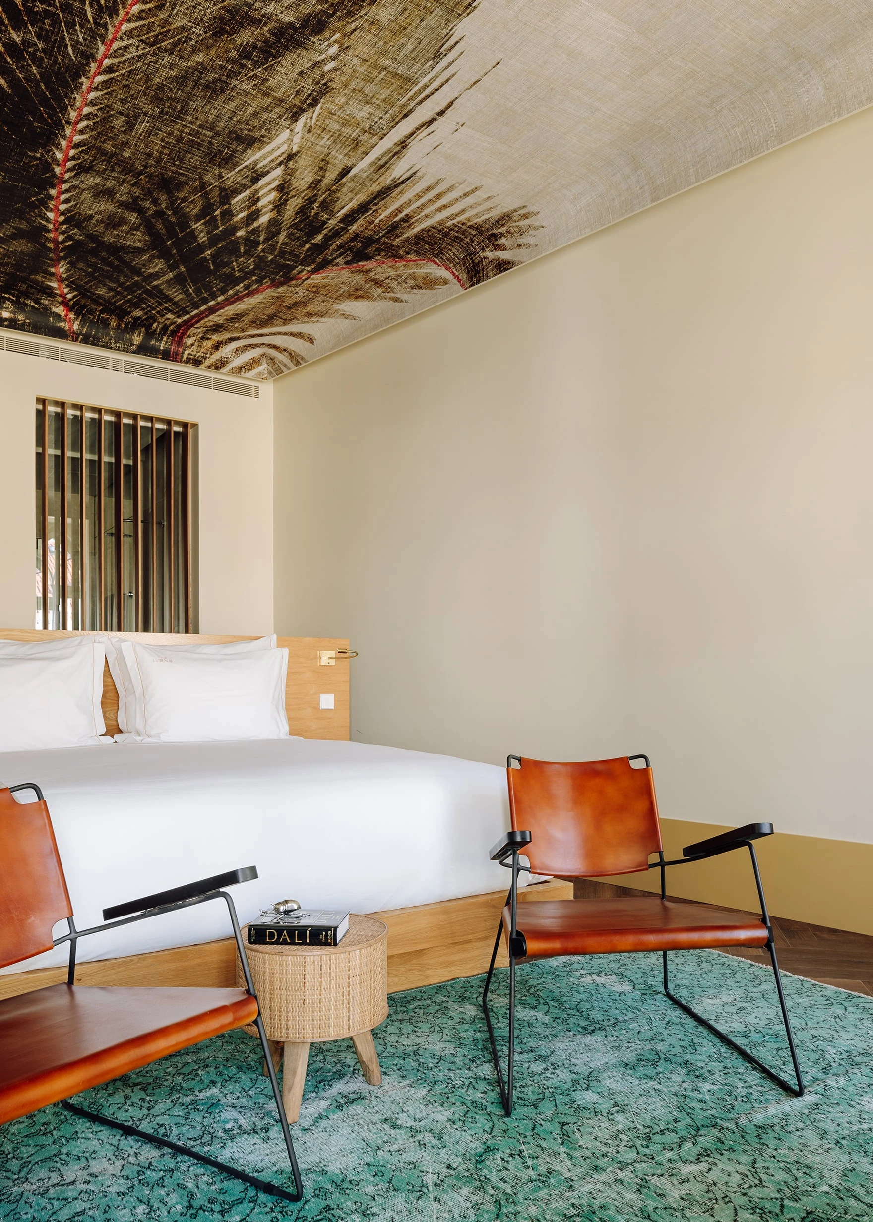 The Ivens by Lázaro Rosa-Violan, photographed by Francisco Nogueira — attic suite with palm-leaf ceiling print, cognac woven-leather sling chairs and jade Berber rug.