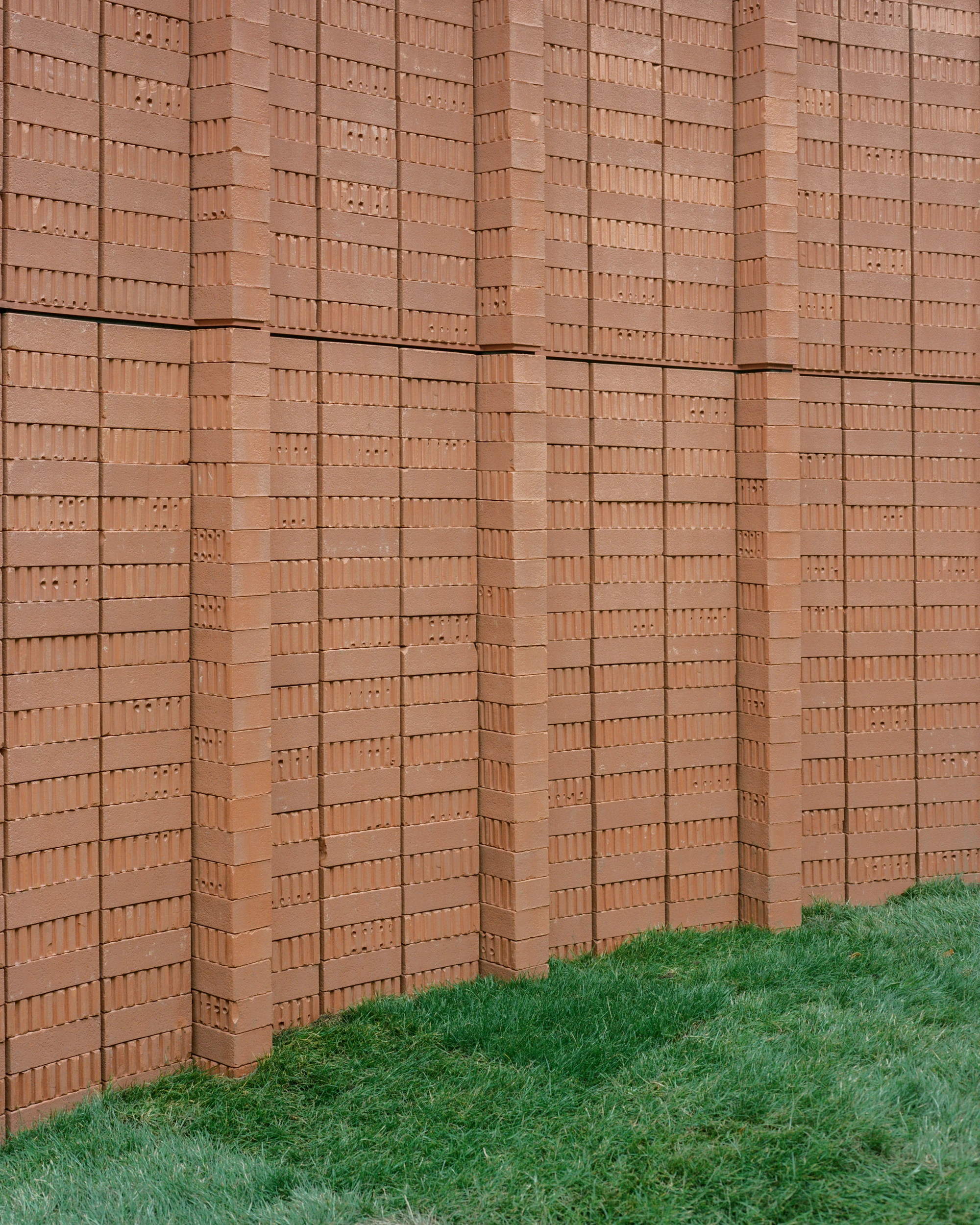 Serpentine Pavilion 2026 by LANZA atelier, photographed by Lorenzo Zandri — detail of the perforated red brick stacked on edge, the hollow faces reading as a vertical weave above the grass.