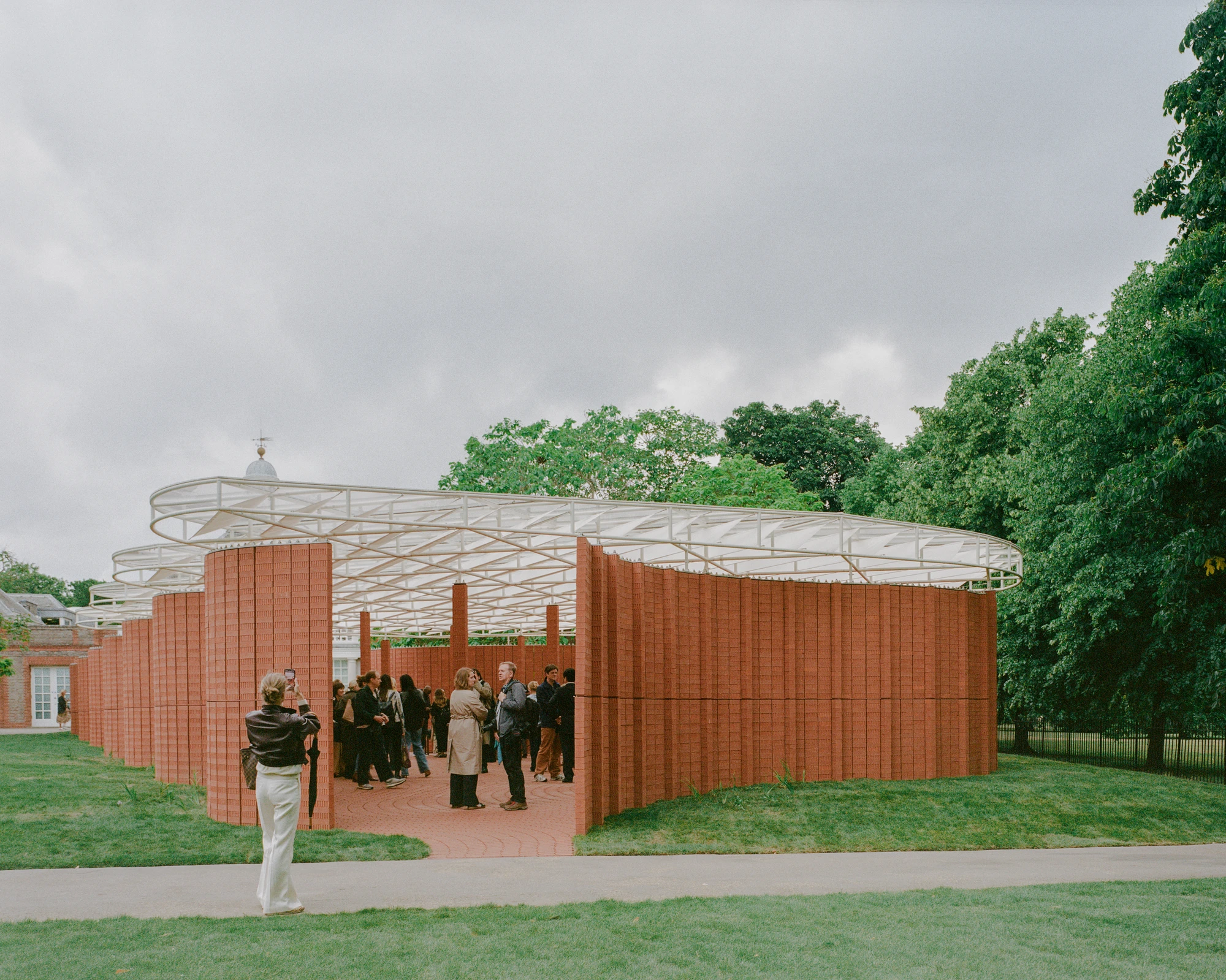 Serpentine Pavilion 2026 by LANZA atelier, photographed by Lorenzo Zandri — opening crowd gathered between the curving brick walls beneath the white tensile roof.