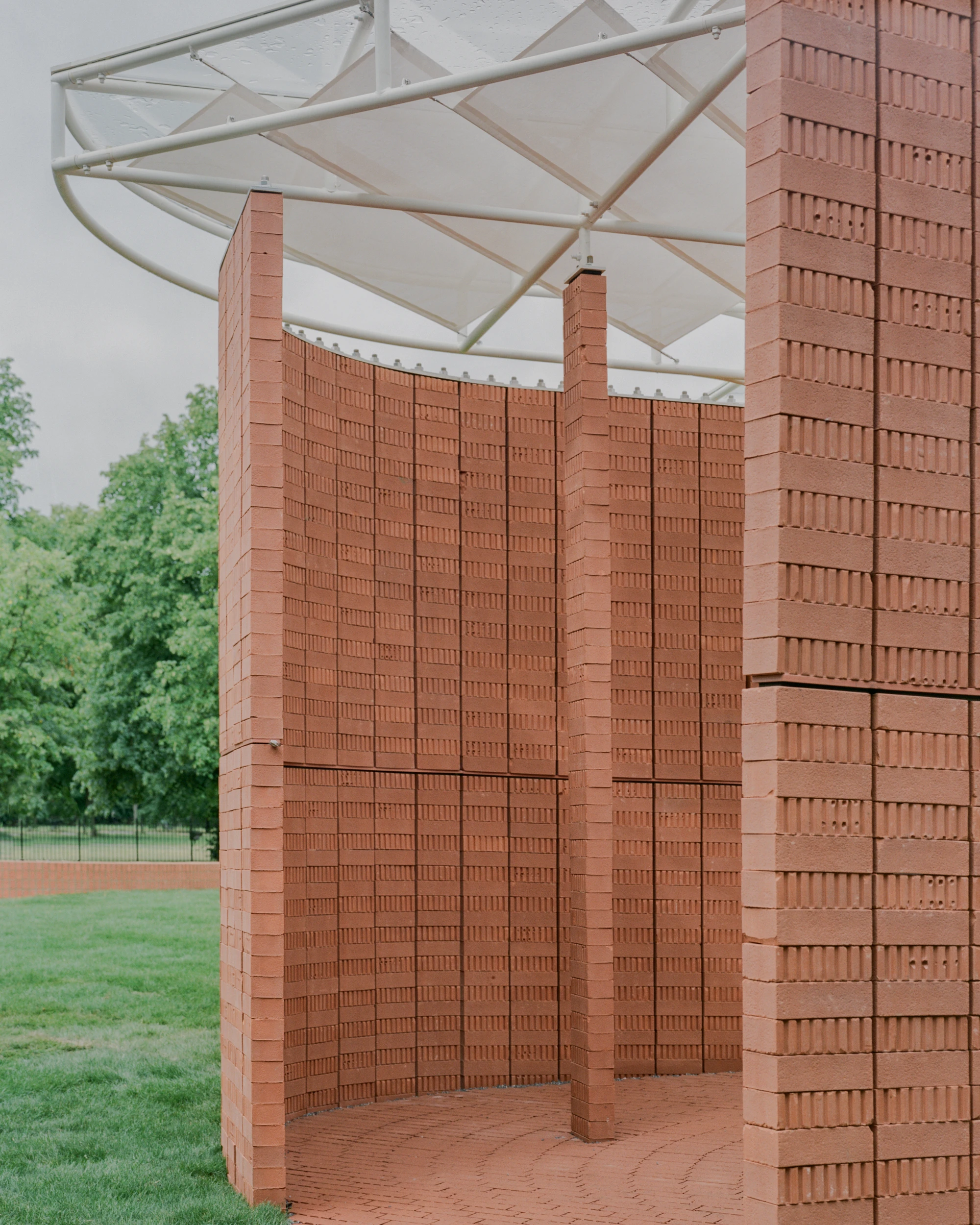 Serpentine Pavilion 2026 by LANZA atelier, photographed by Lorenzo Zandri — close view of a brick column meeting the underside of the translucent fabric roof, with the curving wall behind.