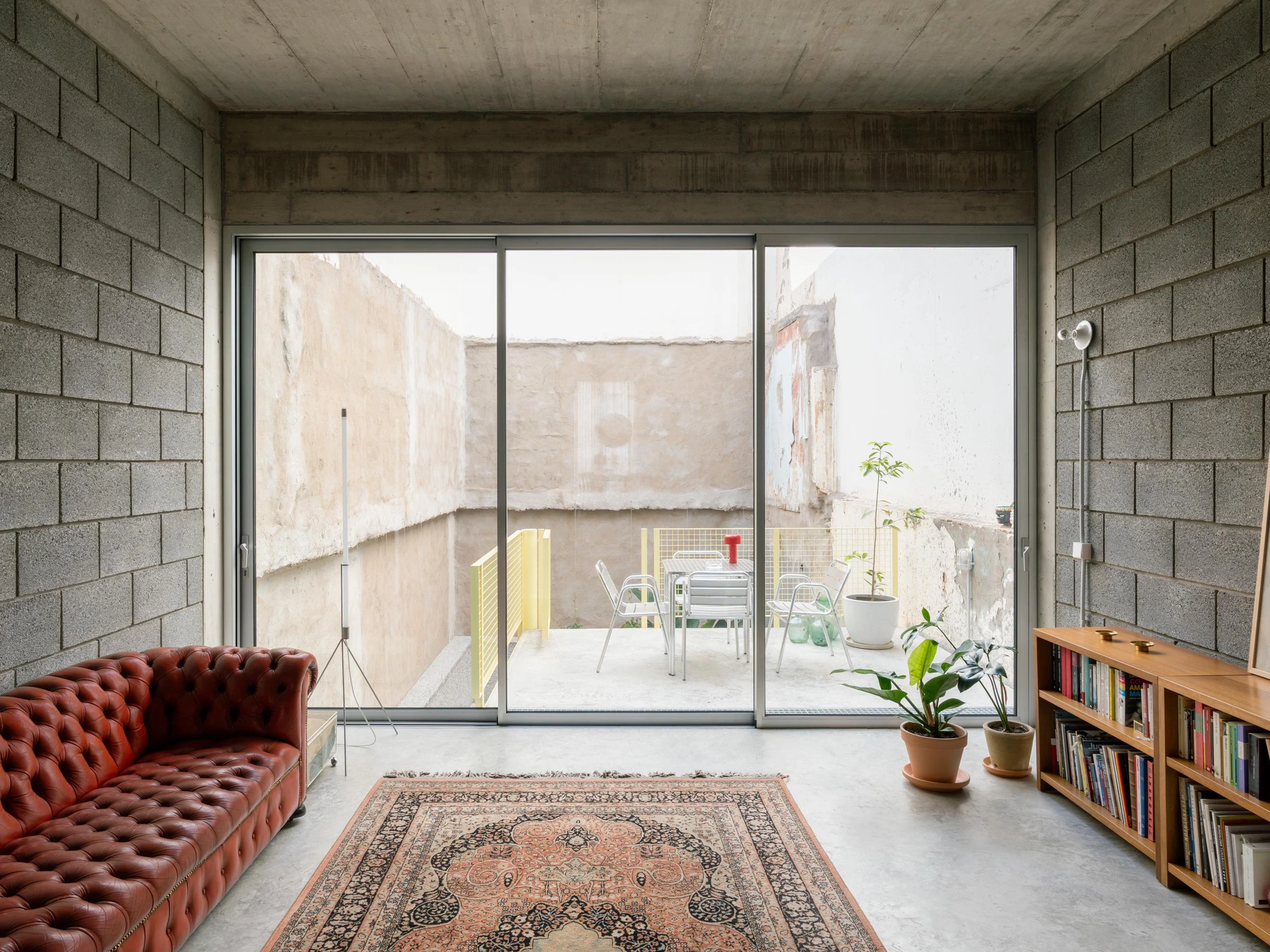 Casa Iriarte by SOCO Estudio, Simone Marcolin: living room opens through full-height sliding glazing to the displaced courtyard, where the raw render of the demolished neighbouring wall is preserved.