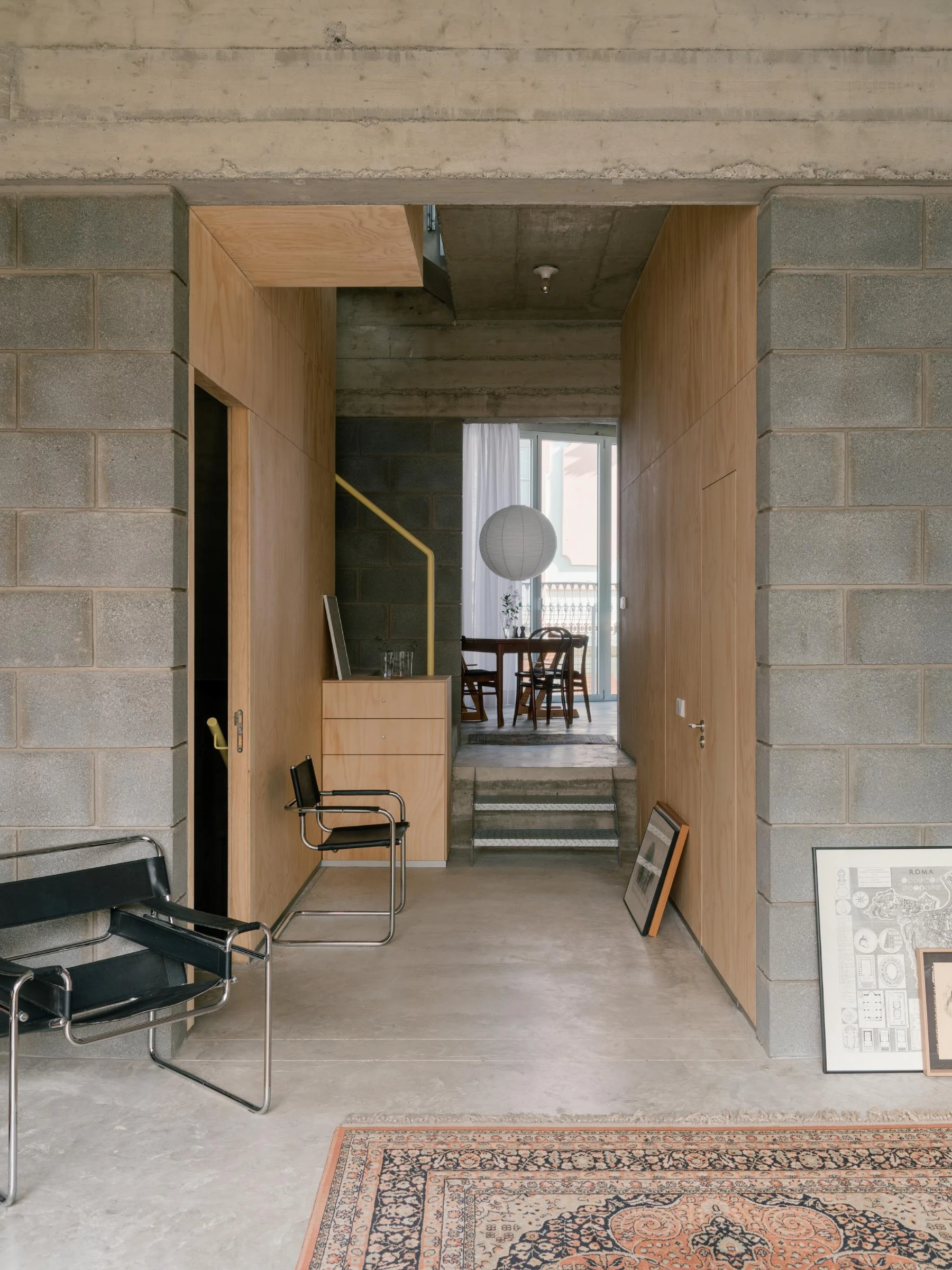 Casa Iriarte by SOCO Estudio, Simone Marcolin: view through a plywood-lined threshold into the dining room, a Wassily chair on a Persian rug, board-formed concrete framing the opening.