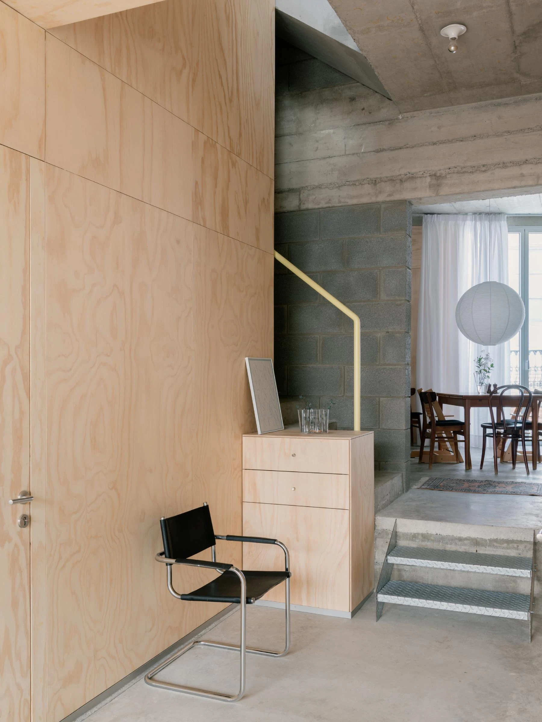 Casa Iriarte by SOCO Estudio, Simone Marcolin: pine plywood wall meets a grey picon block stair shaft, a yellow handrail traces the rise, a black leather cantilever chair waits on polished concrete.