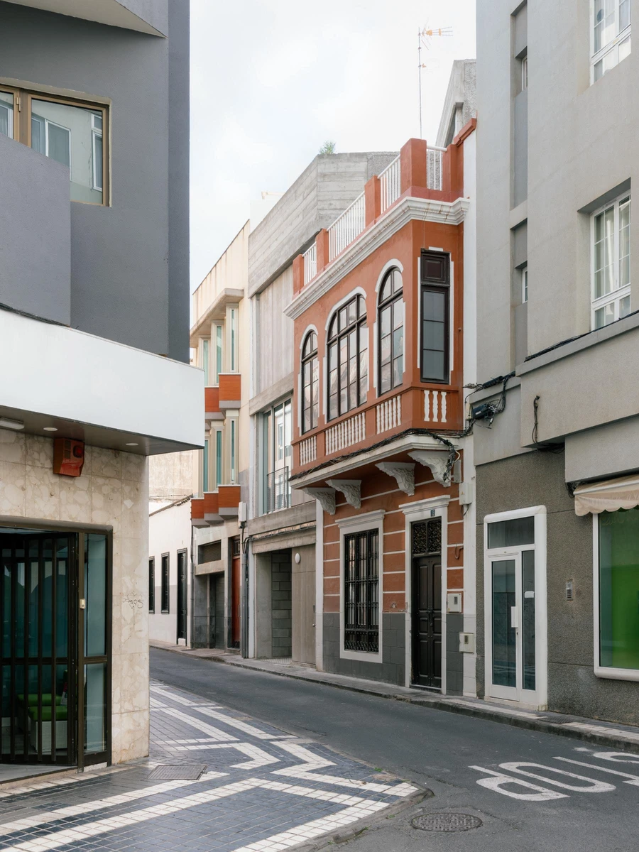 Casa Iriarte by SOCO Estudio, Simone Marcolin: street view from the corner showing the concrete infill rising behind the colonial neighbour's timber balcony.
