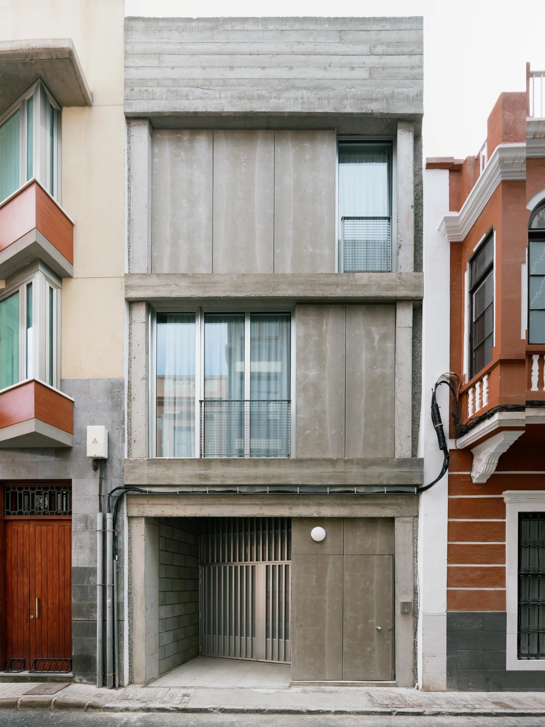 Casa Iriarte by SOCO Estudio, Simone Marcolin: narrow board-formed concrete facade slipped between a red colonial house and a white modern block on a Las Palmas street.