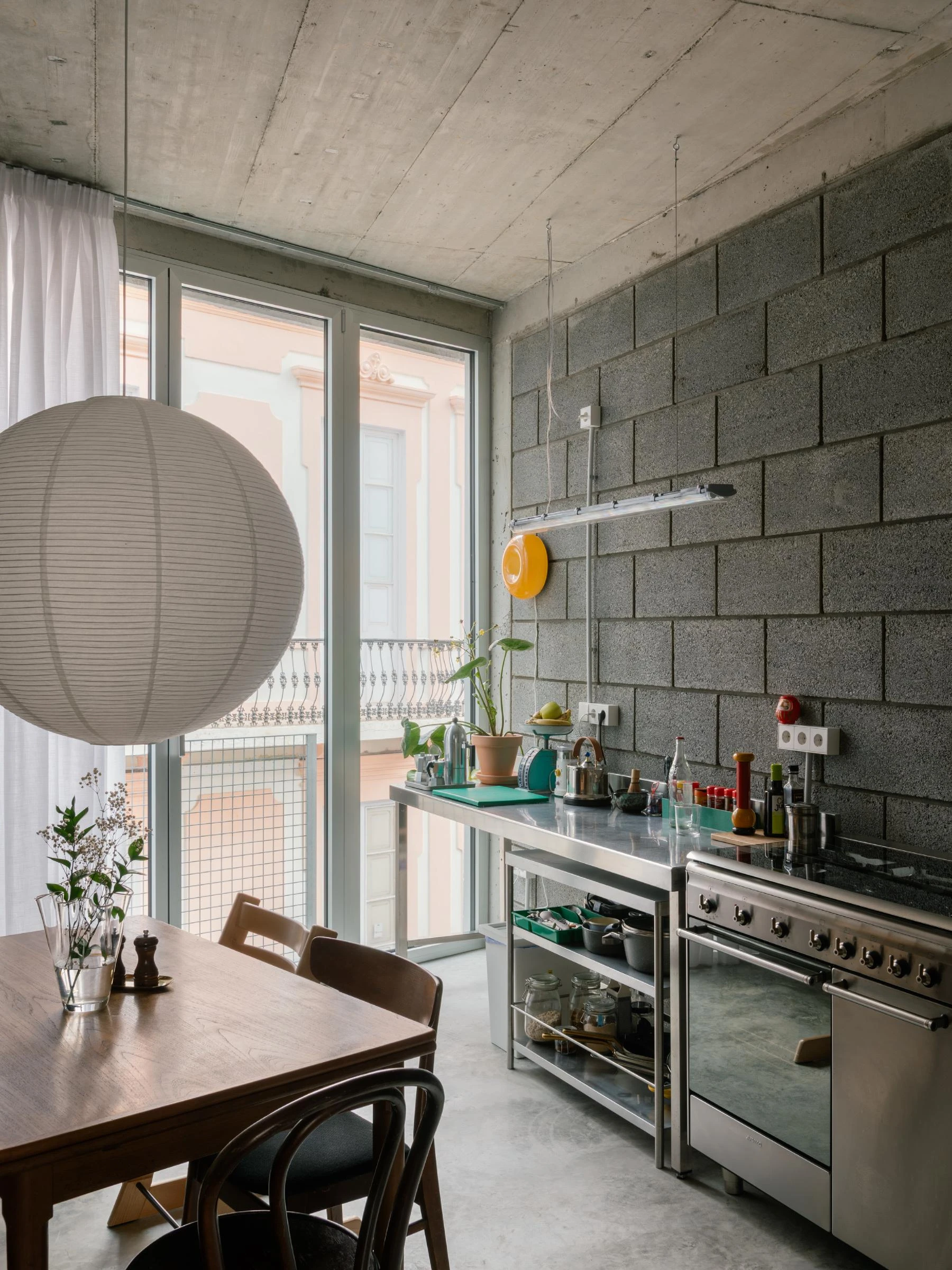 Casa Iriarte by SOCO Estudio, Simone Marcolin: open-plan kitchen with paper lantern, stainless range and picon block wall, dining table set toward the street balcony beyond.