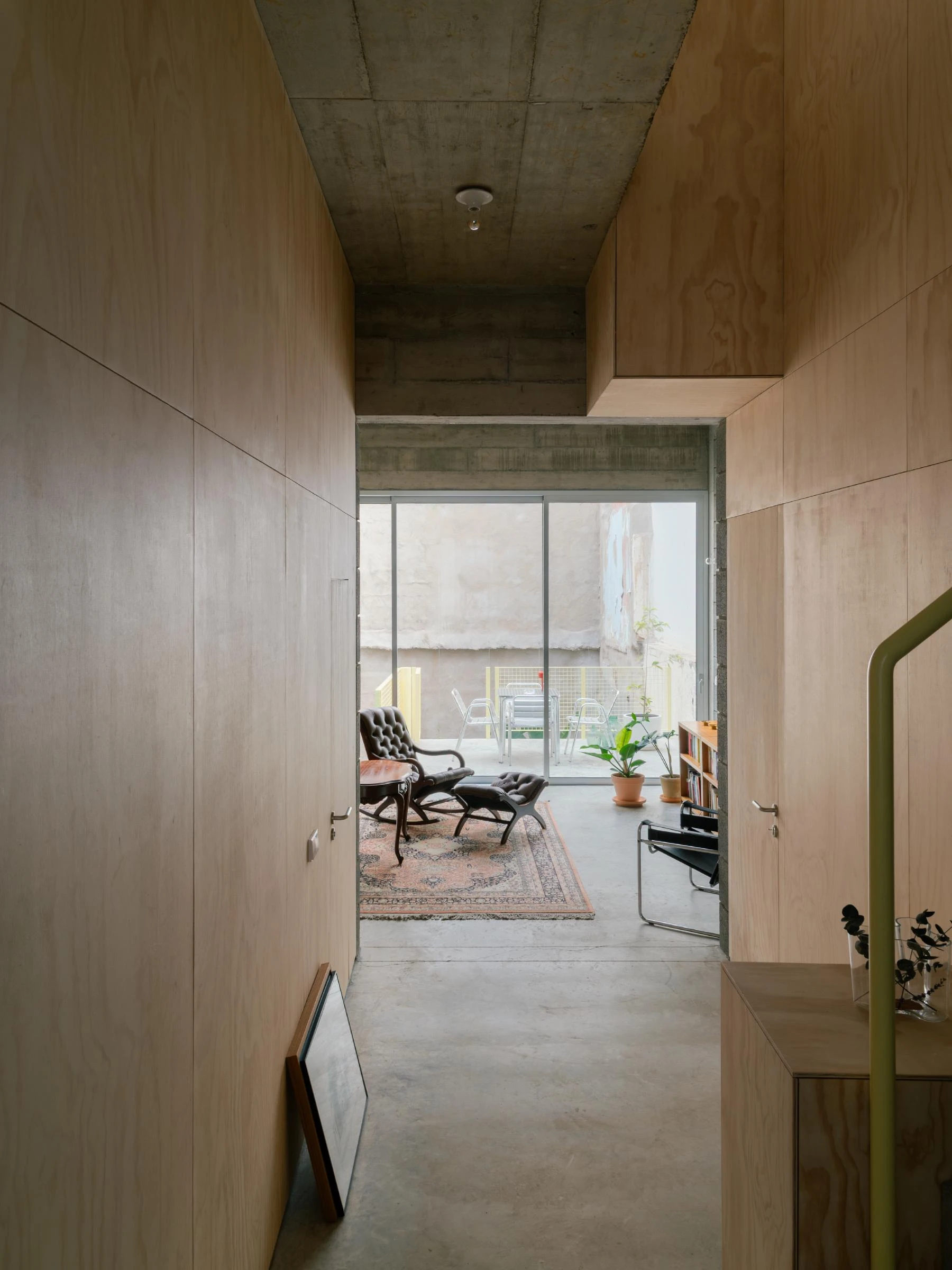 Casa Iriarte by SOCO Estudio, Simone Marcolin: plywood-lined corridor opens to a living room on the courtyard, antique rocker and Wassily chair on a Persian rug.