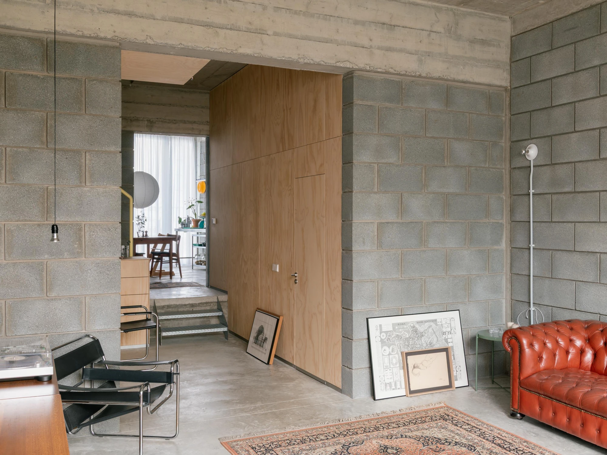 Casa Iriarte by SOCO Estudio, Simone Marcolin: living room interior with a red leather Chesterfield against grey picon block, a Wassily chair and framed prints leaned at the floor.