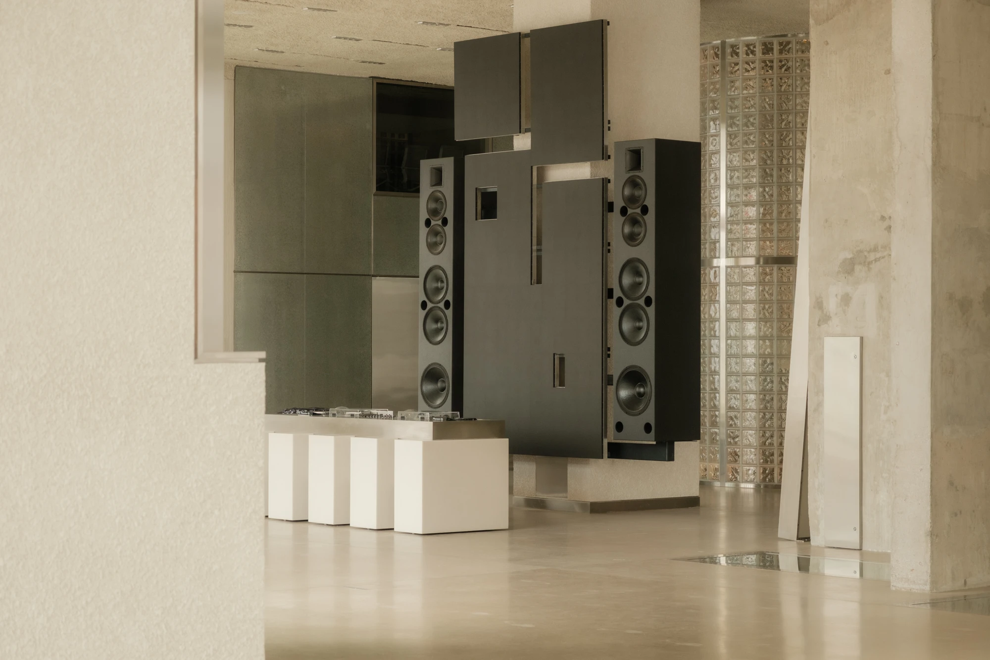 OUNASS STAGE by VAUST, photographed by Nicolas Quiniou — the hi-fi tower of black professional studio monitors stacked vertically beside the DJ booth, framed by a glass-block silo and a board-formed concrete wall.
