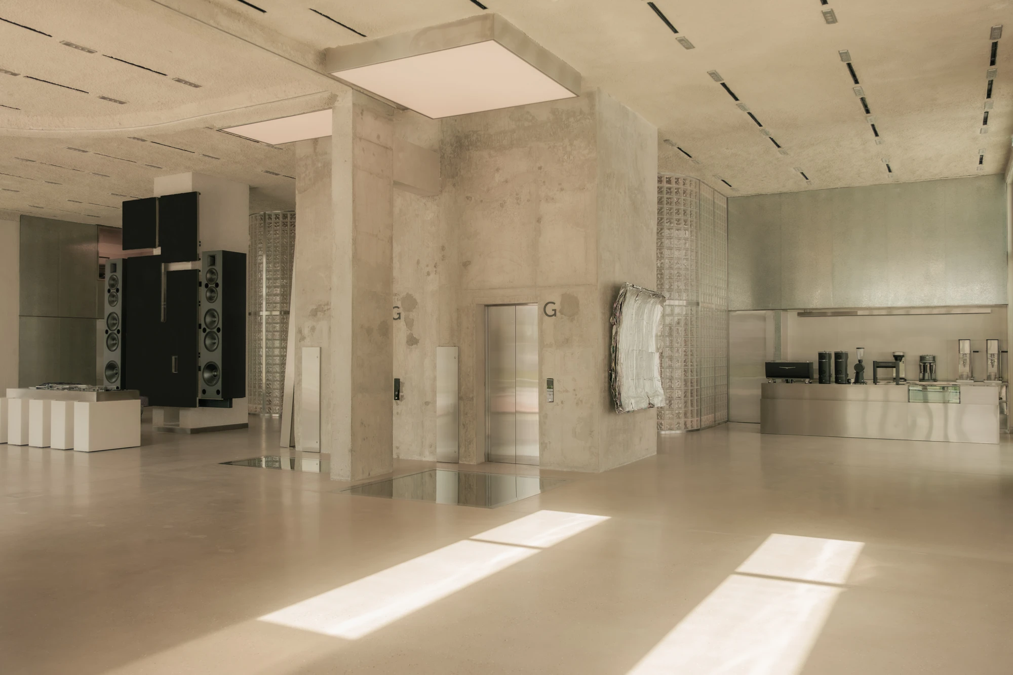OUNASS STAGE by VAUST, photographed by Nicolas Quiniou — wide afternoon view of the floor with low sun raking across the polished concrete past board-formed columns, sand pits set into the slab and the hi-fi tower in the distance.