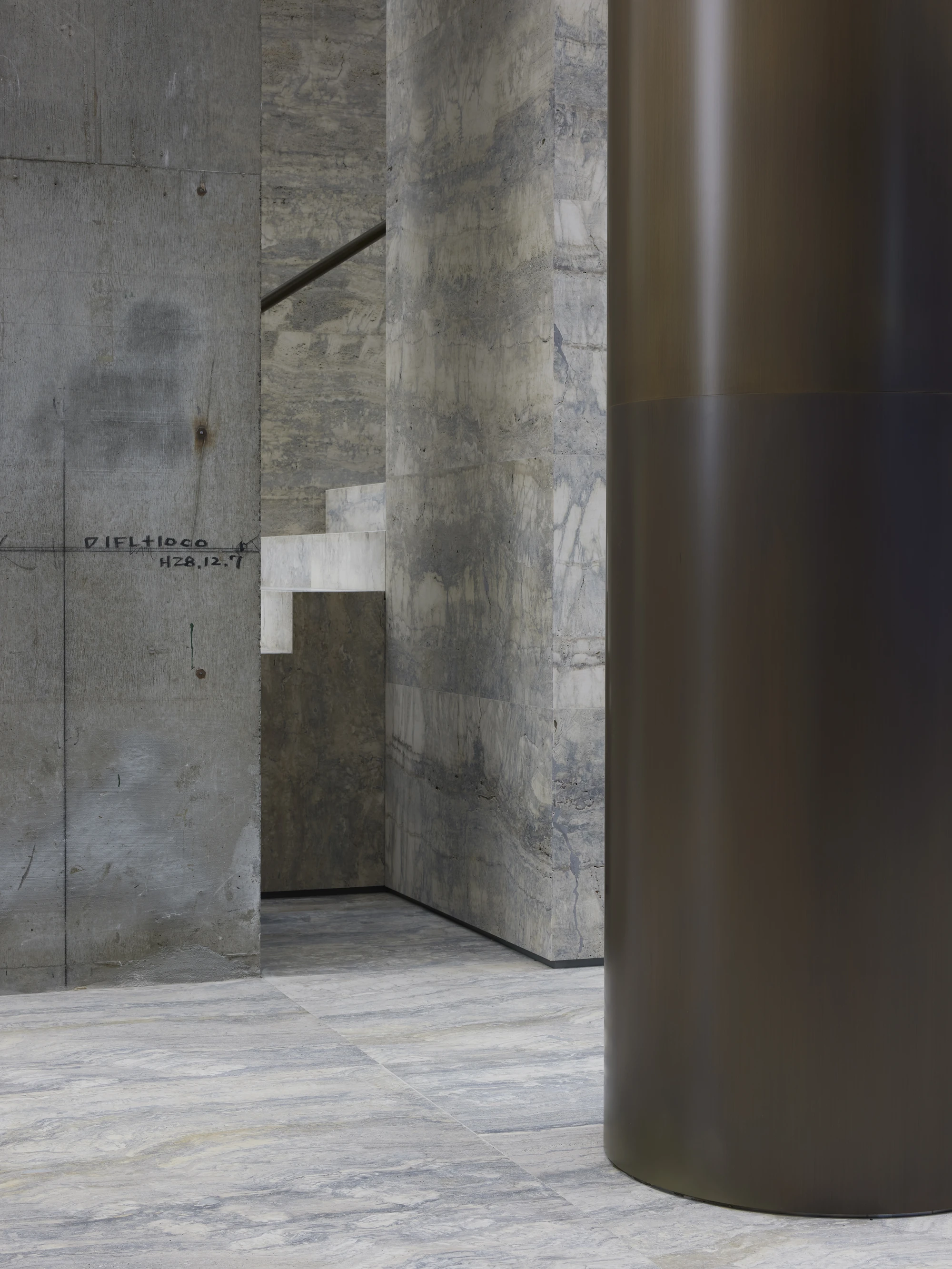 Jil Sander Flagship Store Ginza by Casper Mueller Kneer Architects, photographed by Paul Riddle — patinated brass column meets board-formed concrete wall inscribed with Japanese construction marks, travertine floor below.