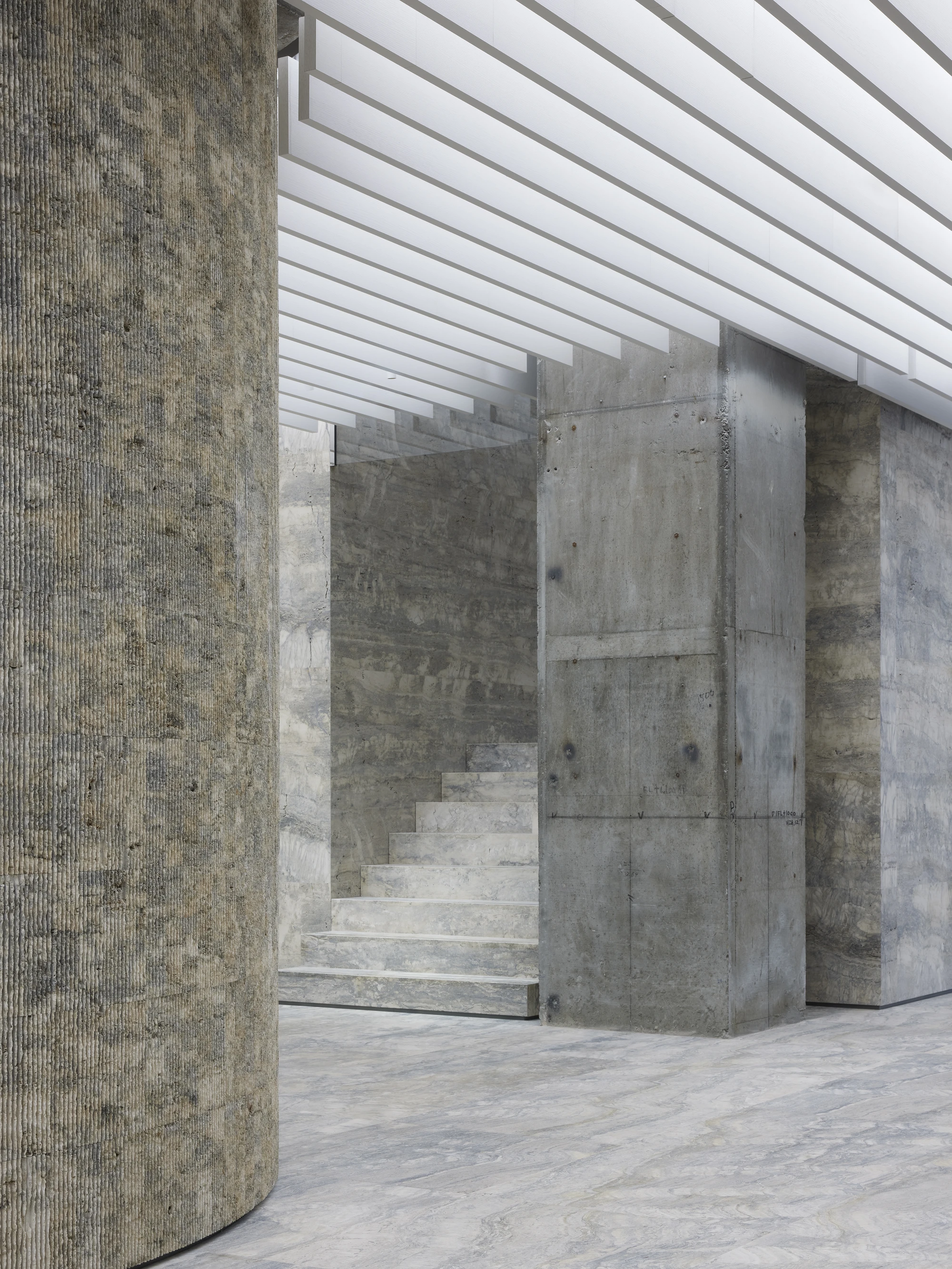 Jil Sander Flagship Store Ginza by Casper Mueller Kneer Architects, photographed by Paul Riddle — stair rising between the textured rotunda and a board-formed concrete pillar under a white slatted ceiling.