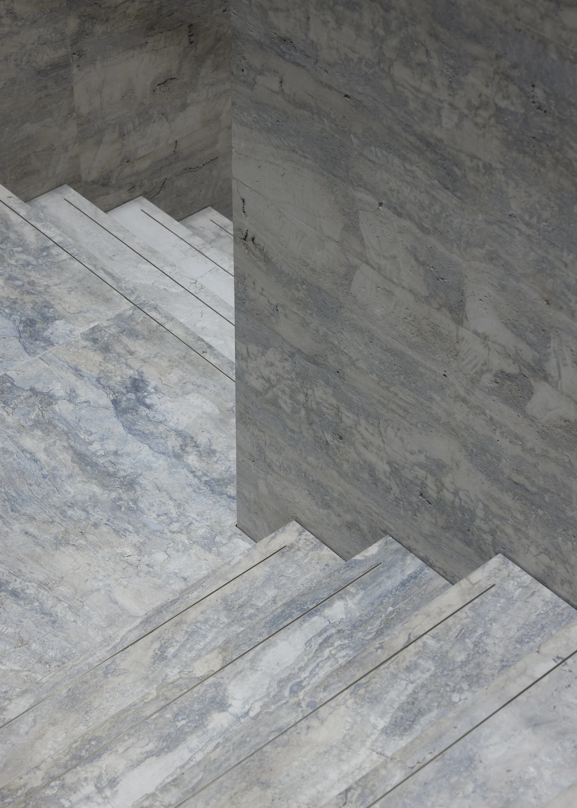 Jil Sander Flagship Store Ginza by Casper Mueller Kneer Architects, photographed by Paul Riddle — abstract crop of silver-blue travertine stairs meeting a travertine-clad wall, raking daylight from above.