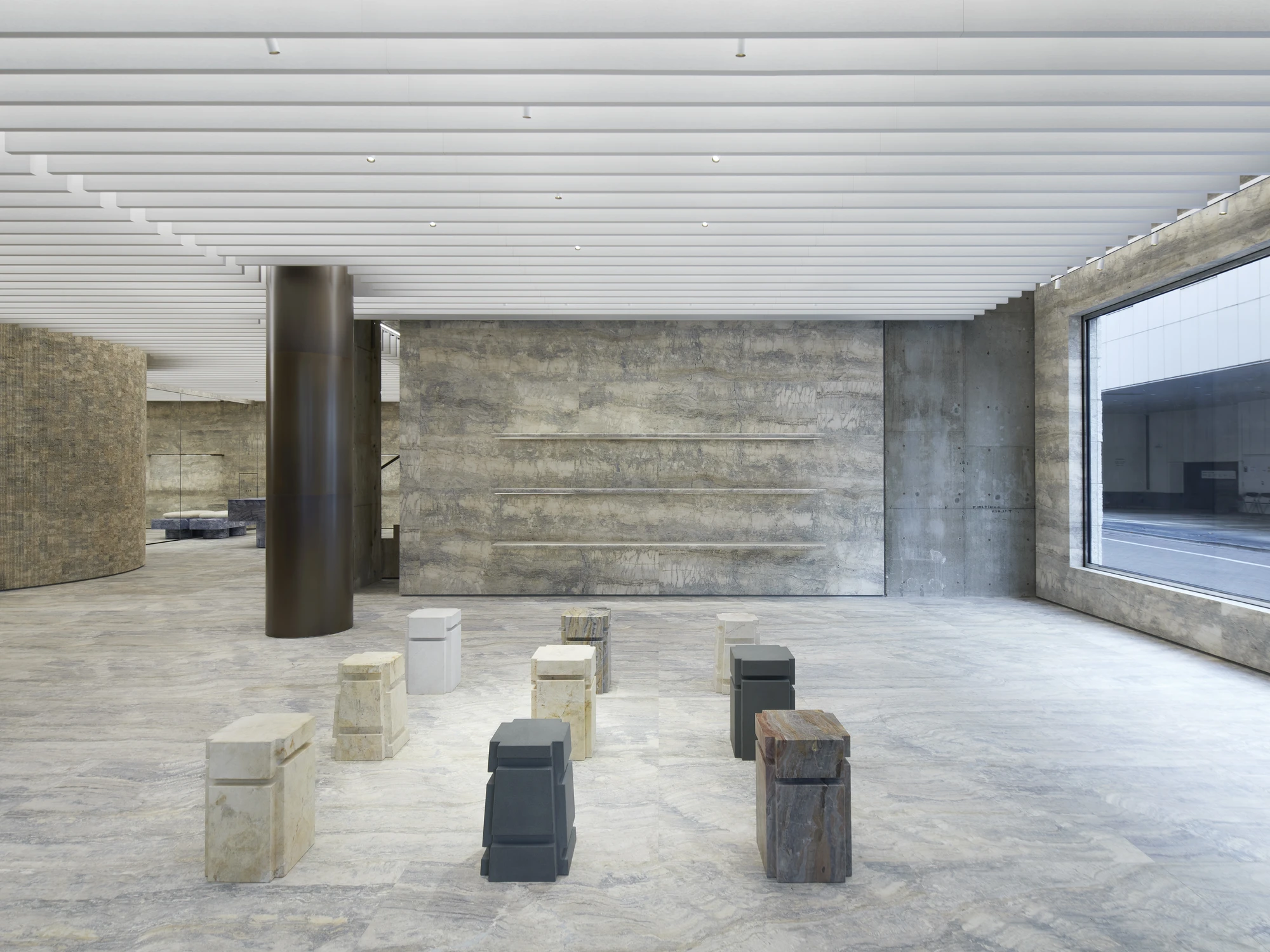 Jil Sander Flagship Store Ginza by Casper Mueller Kneer Architects, photographed by Paul Riddle — ground-floor exhibition room with Rachel Whiteread marble sculptures arranged on the travertine floor against a board-formed concrete wall with cut shelf ins