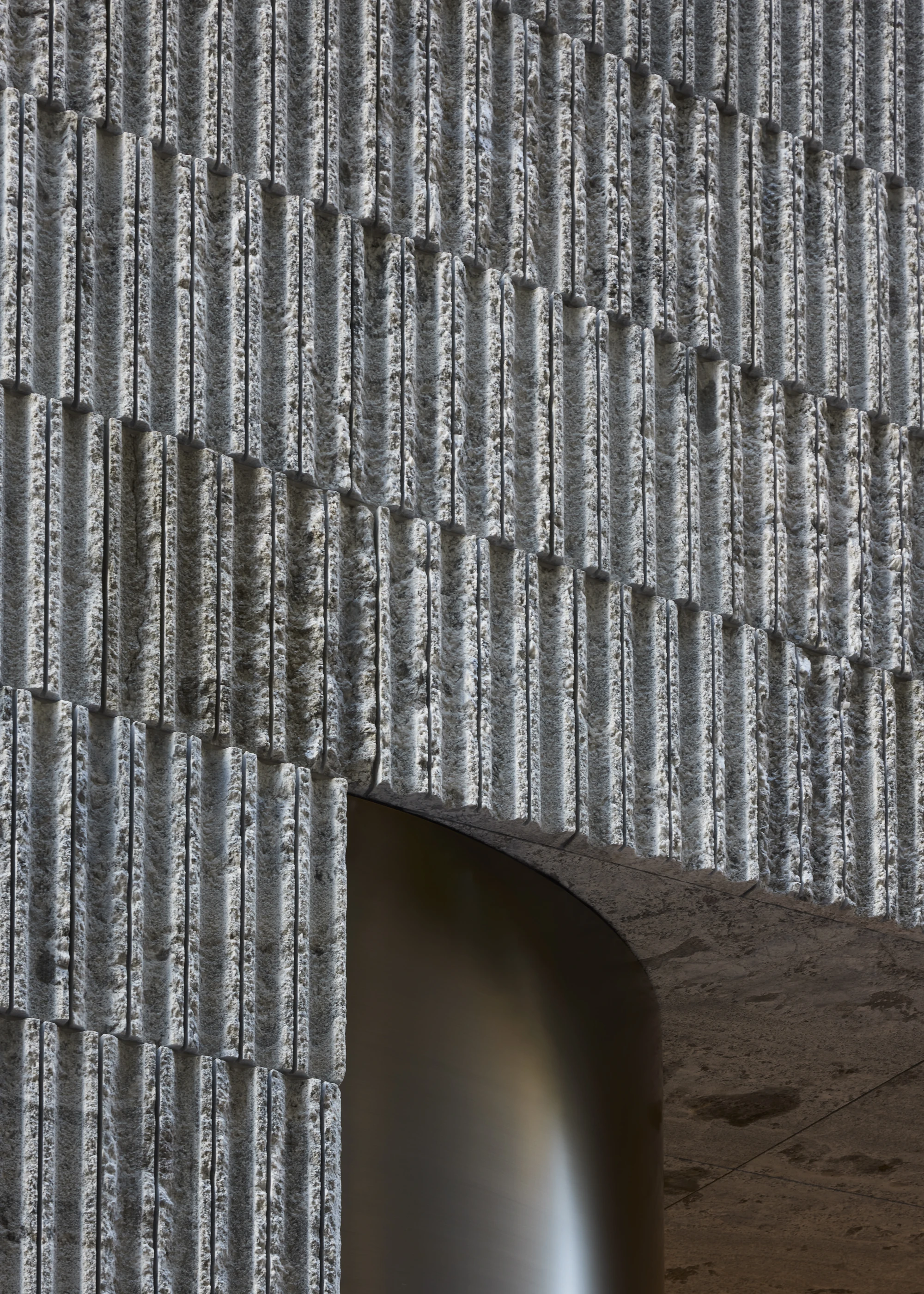 Jil Sander Flagship Store Ginza by Casper Mueller Kneer Architects, photographed by Paul Riddle — close-up of the staggered grey-green granite facade tiles, vertically scored and stacked above the brass-rimmed entry curve.