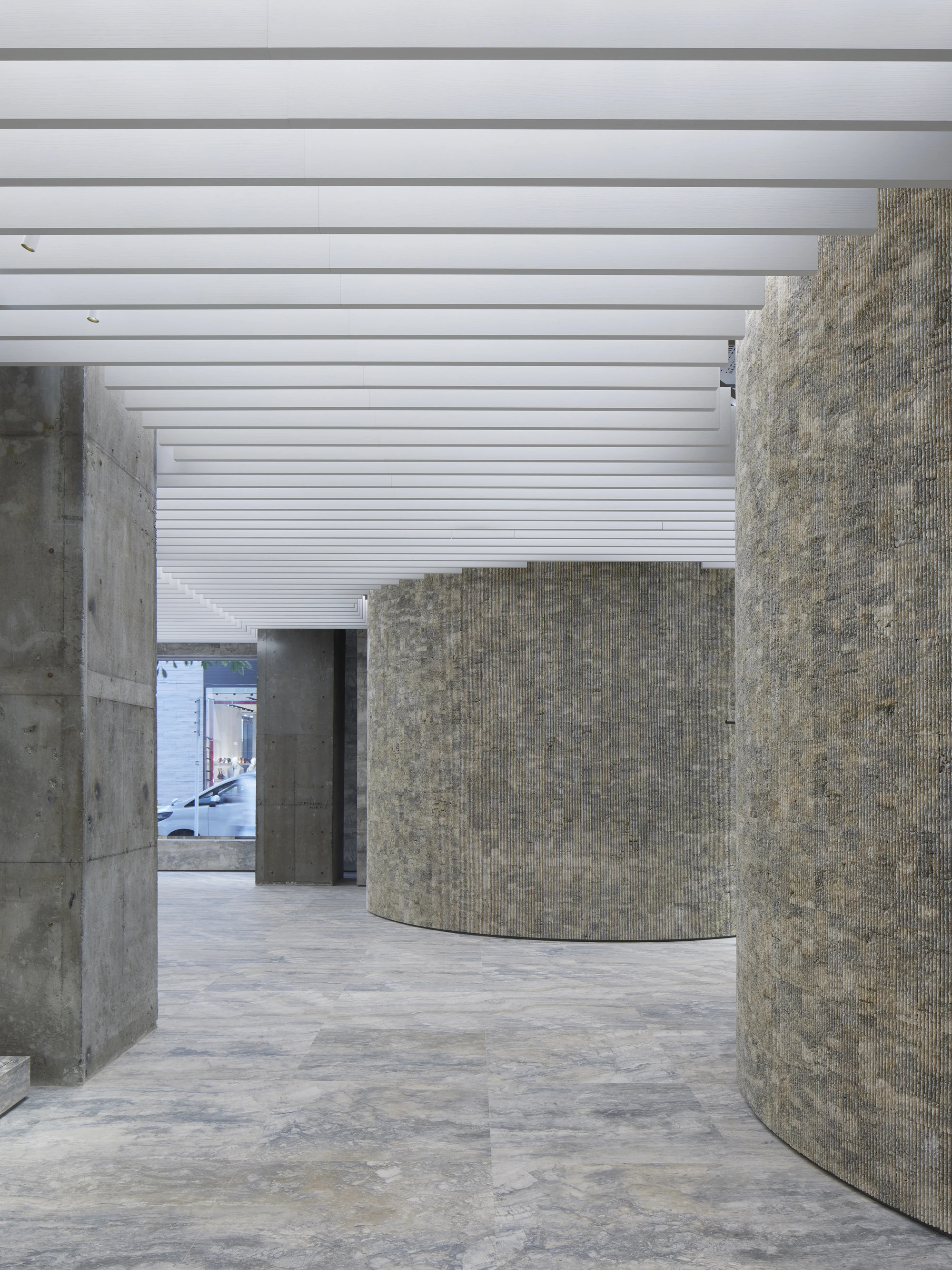Jil Sander Flagship Store Ginza by Casper Mueller Kneer Architects, photographed by Paul Riddle — two rotunda volumes set into the plan, pressed mineral aggregate beside board-formed concrete, daylight entering from the street.