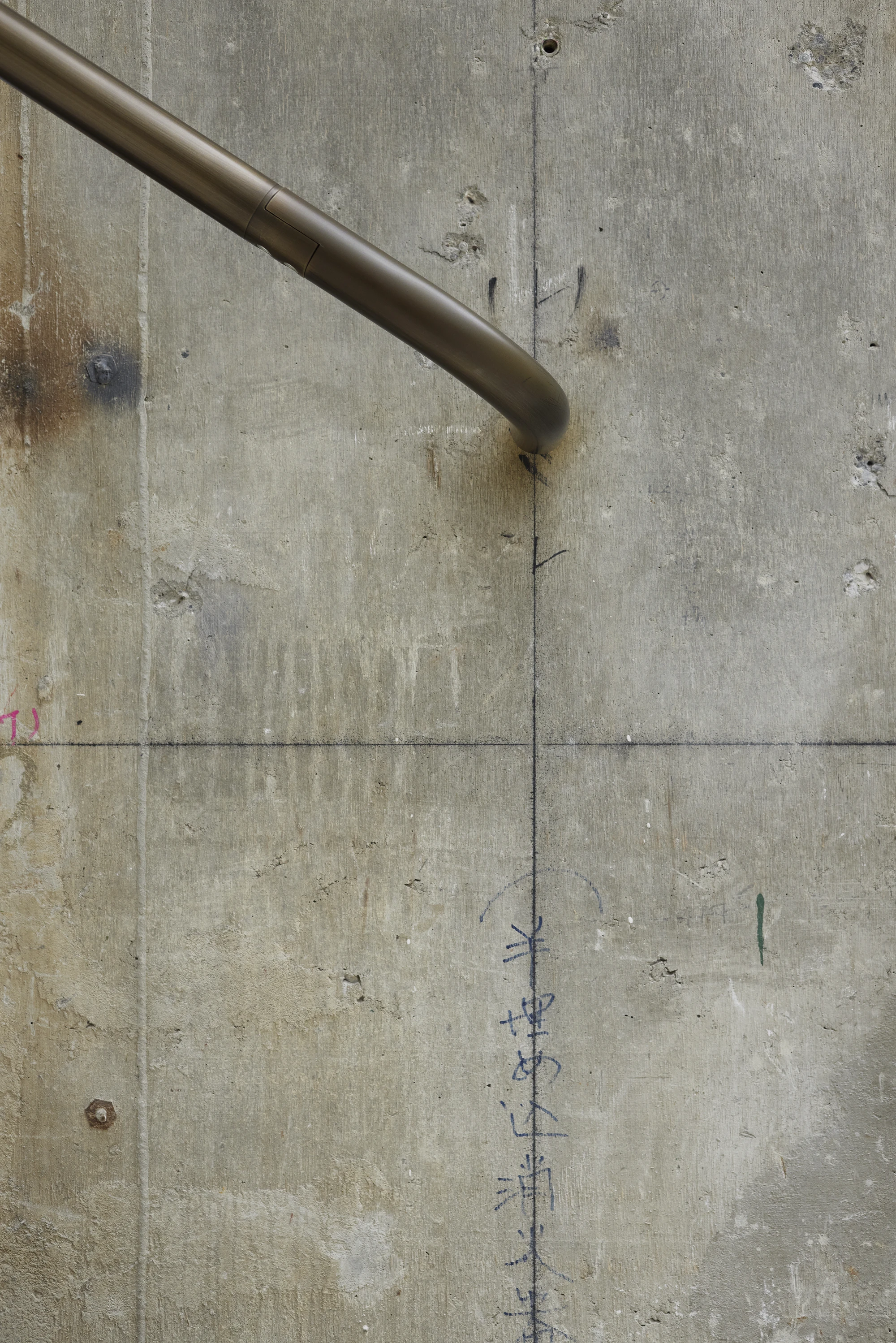 Jil Sander Flagship Store Ginza by Casper Mueller Kneer Architects, photographed by Paul Riddle — close-up of preserved board-formed concrete with Japanese construction notations, pink and blue chalk marks, brass handrail terminus.