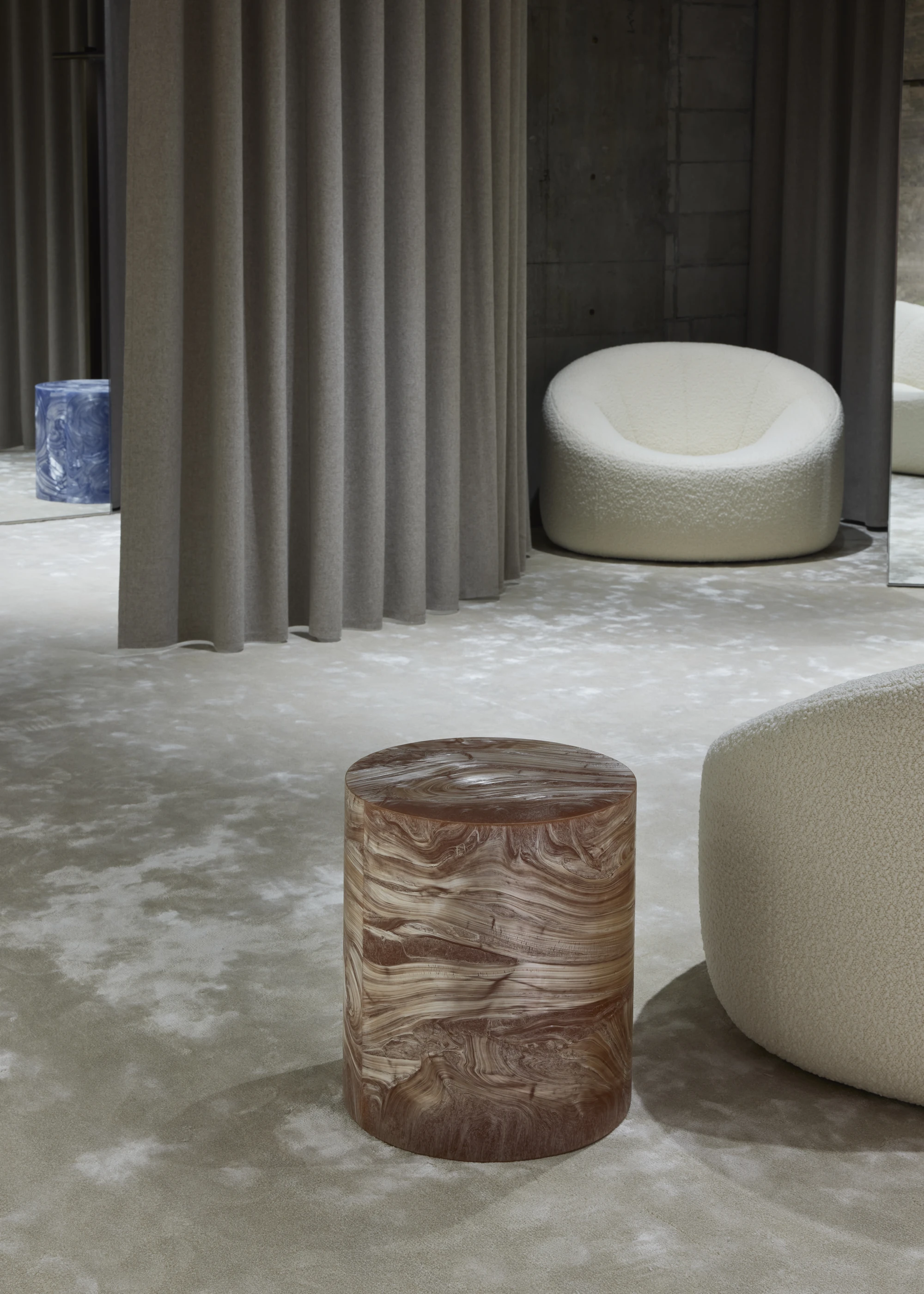 Jil Sander Flagship Store Ginza by Casper Mueller Kneer Architects, photographed by Paul Riddle — pleated felt curtain frames a marbled timber drum stool, a cream boucle bench, and a deep-blue marble side table.