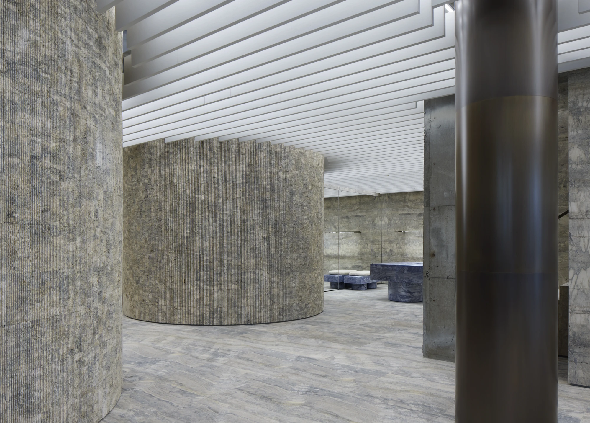 Jil Sander Flagship Store Ginza by Casper Mueller Kneer Architects, photographed by Paul Riddle — pressed mineral-aggregate rotunda anchored between board-formed concrete walls and a patinated brass column.