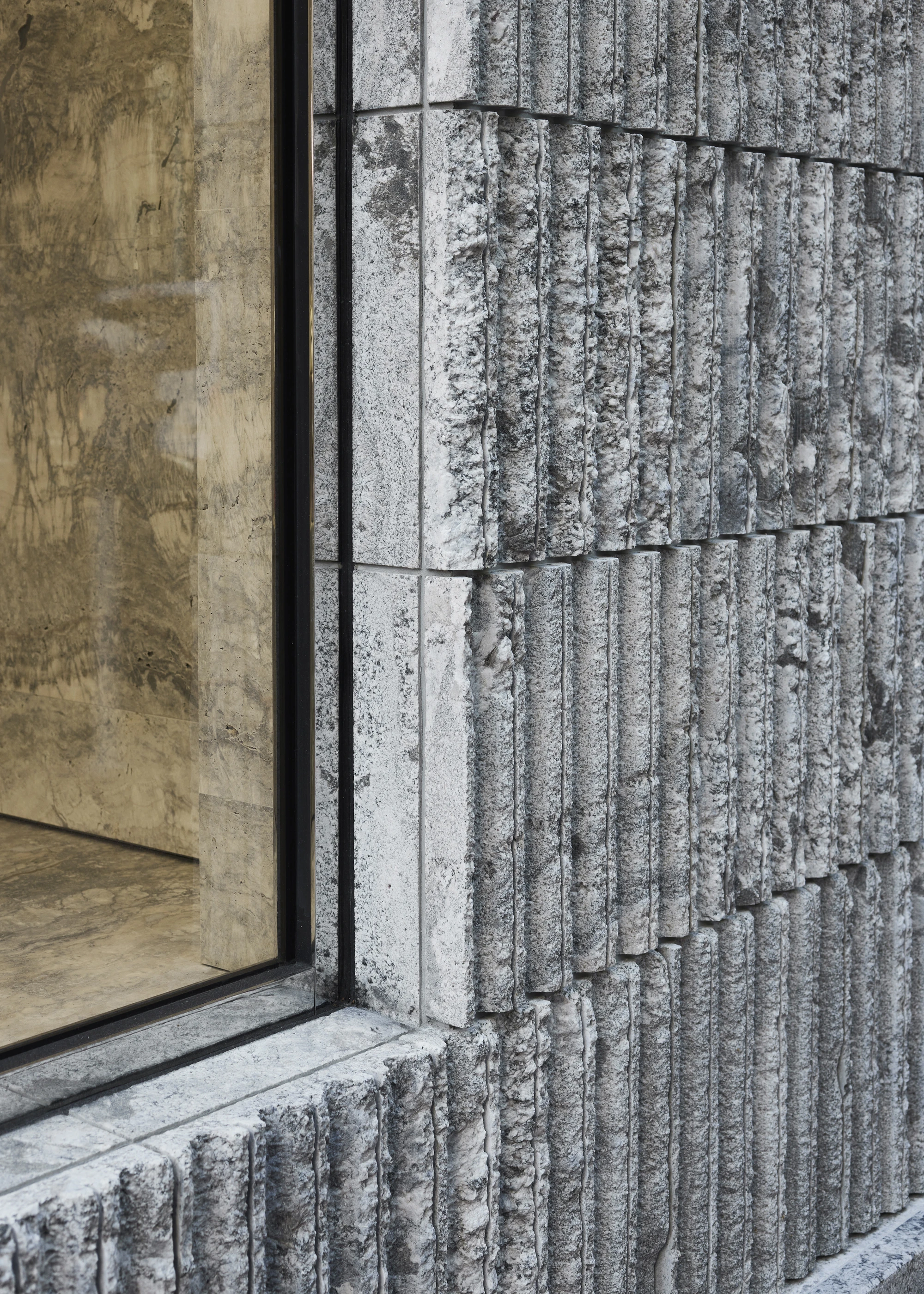 Jil Sander Flagship Store Ginza by Casper Mueller Kneer Architects, photographed by Paul Riddle — corner detail where the scored granite facade meets the brass-framed window onto the travertine-clad interior.