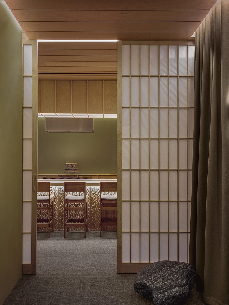 Hos Bobby by NÆRSTUDIO, photographed by Hugo Lütcherath — View through the timber-framed entry toward the omakase counter, where timber stools stand against a carved, backlit counter front.
