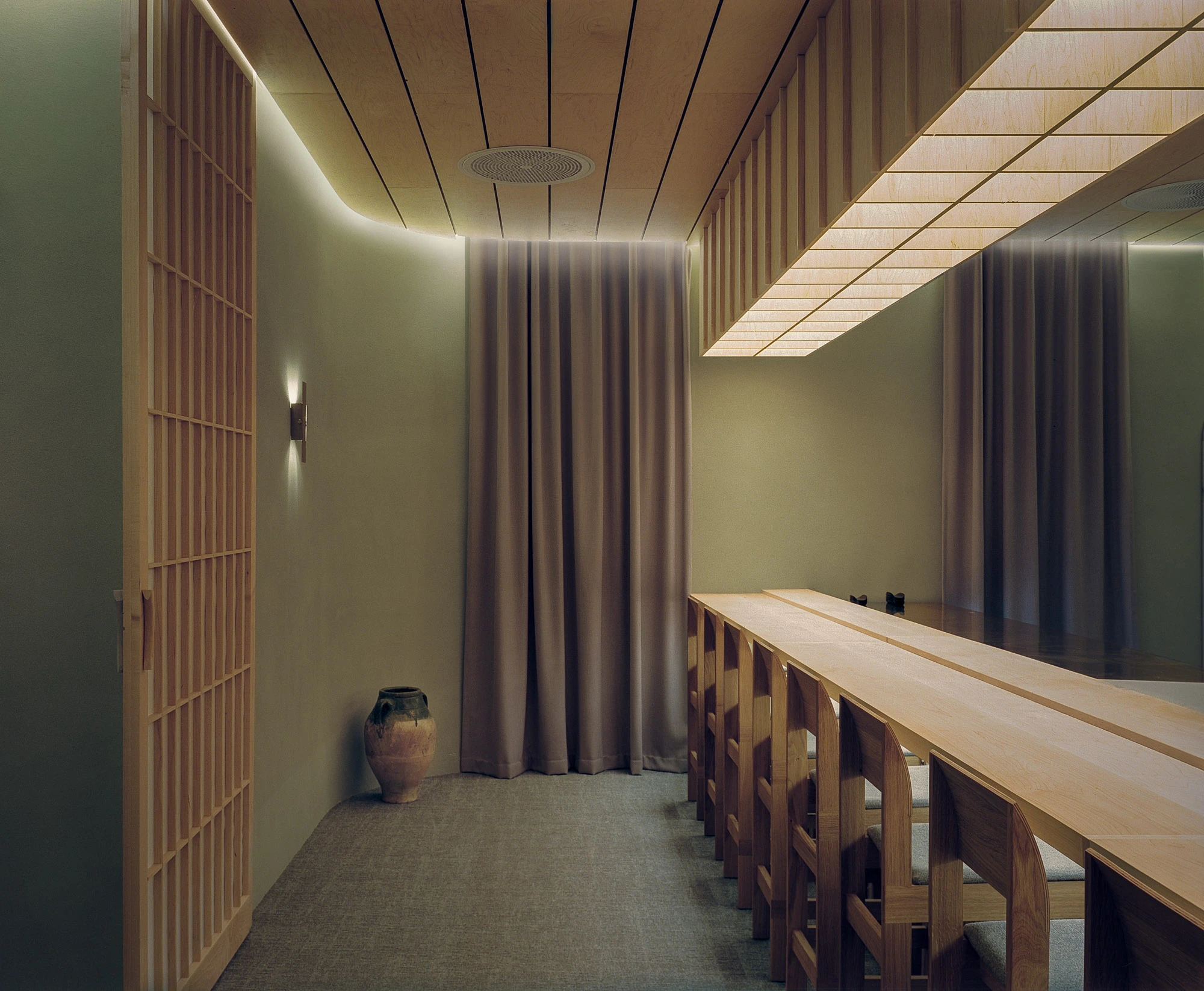 Hos Bobby by NÆRSTUDIO, photographed by Hugo Lütcherath — The second dining room, where a backlit canopy of veneer panels hangs above a long timber counter and arch-legged stools.