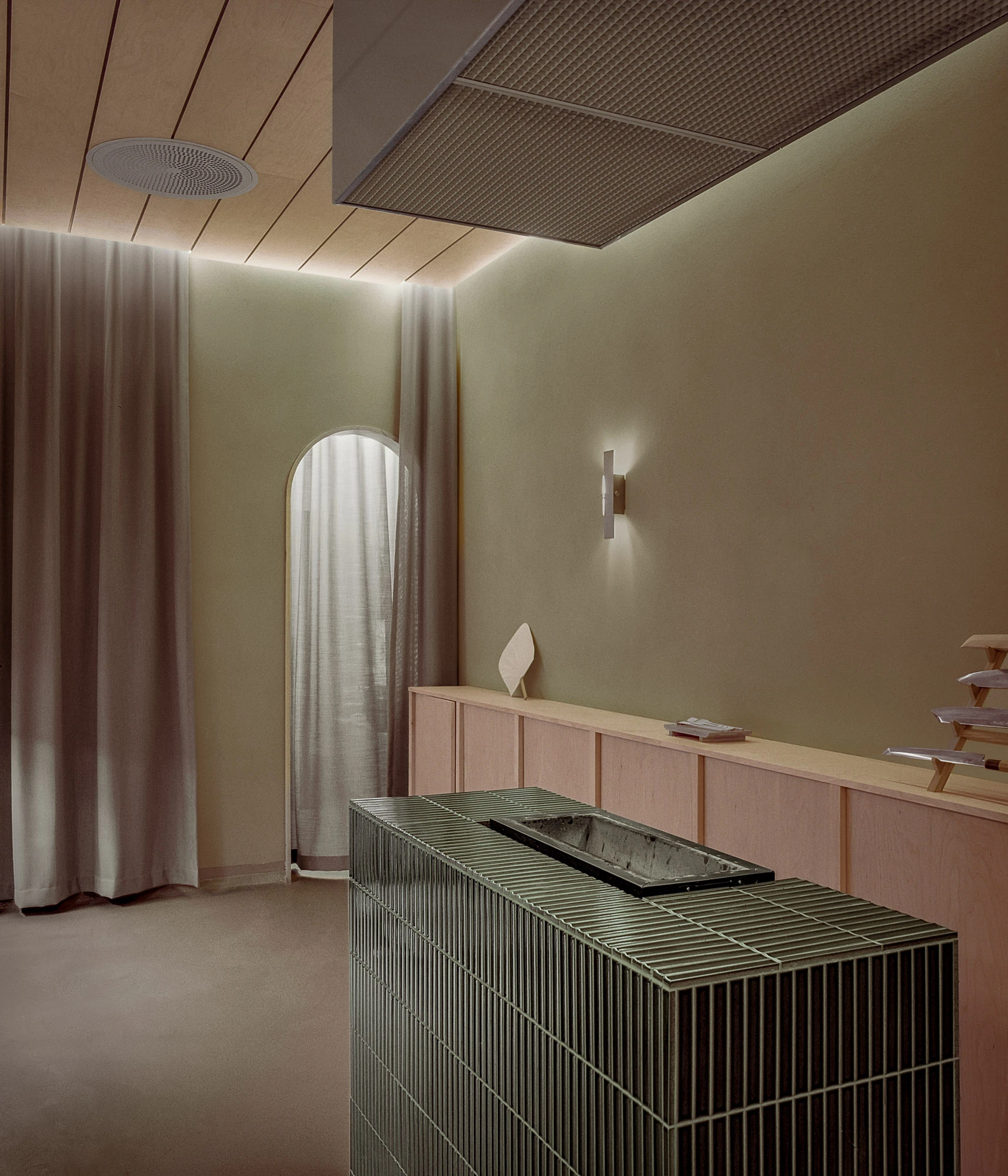 Hos Bobby by NÆRSTUDIO, photographed by Hugo Lütcherath — The prep kitchen's freestanding island wrapped in moss-green finger tiles, with a sunken stainless basin and knives racked behind.