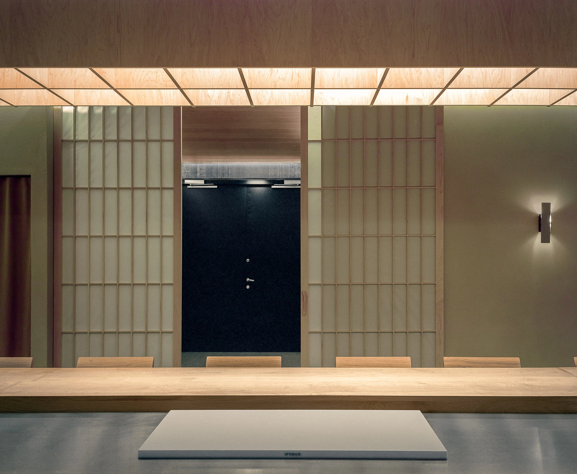 Hos Bobby by NÆRSTUDIO, photographed by Hugo Lütcherath — Sliding shoji-style screens flank a dark door behind the counter, a white serving board set on brushed steel.