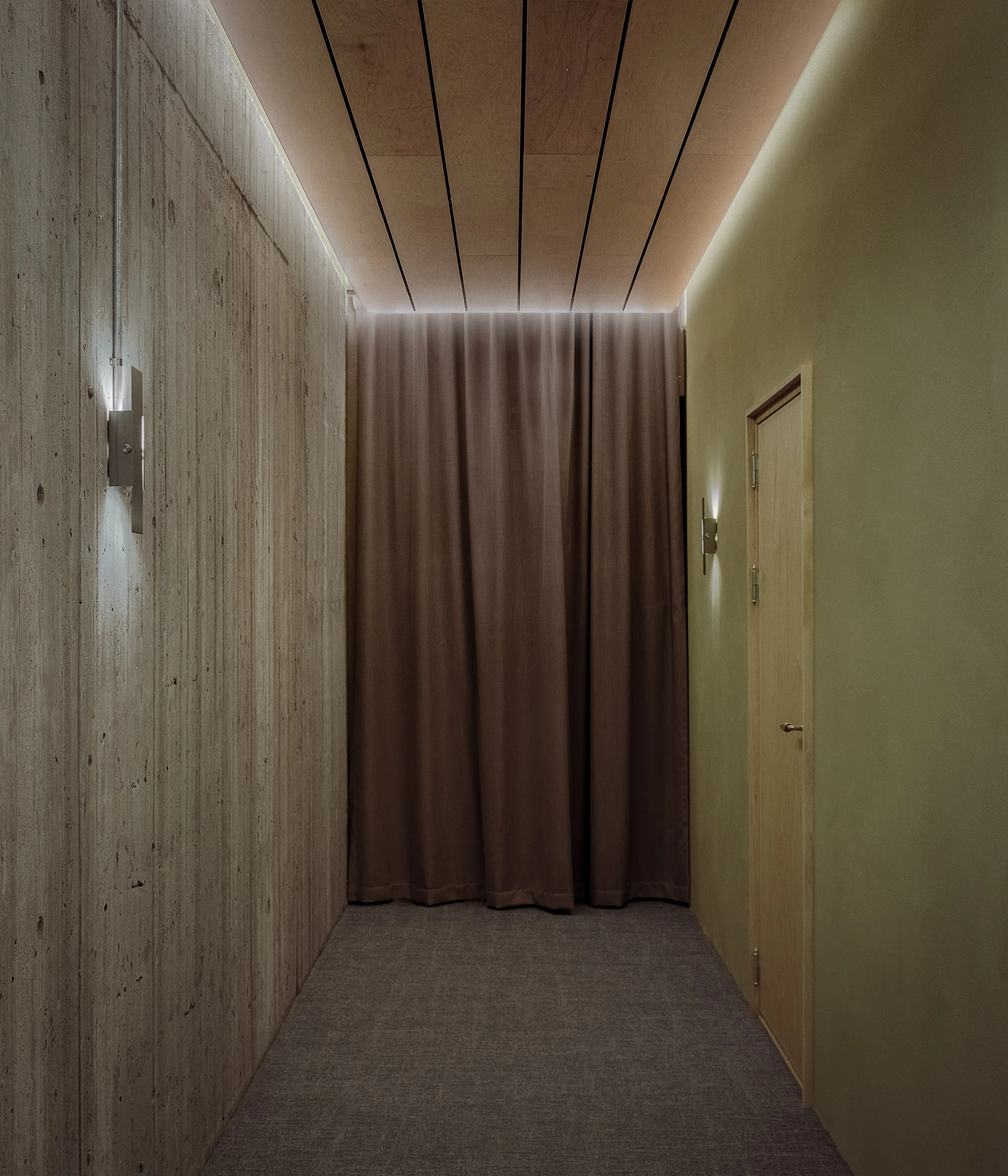 Hos Bobby by NÆRSTUDIO, photographed by Hugo Lütcherath — A corridor pairs the museum's board-formed concrete with green clay plaster, pale timber boards and a cove of concealed light overhead.