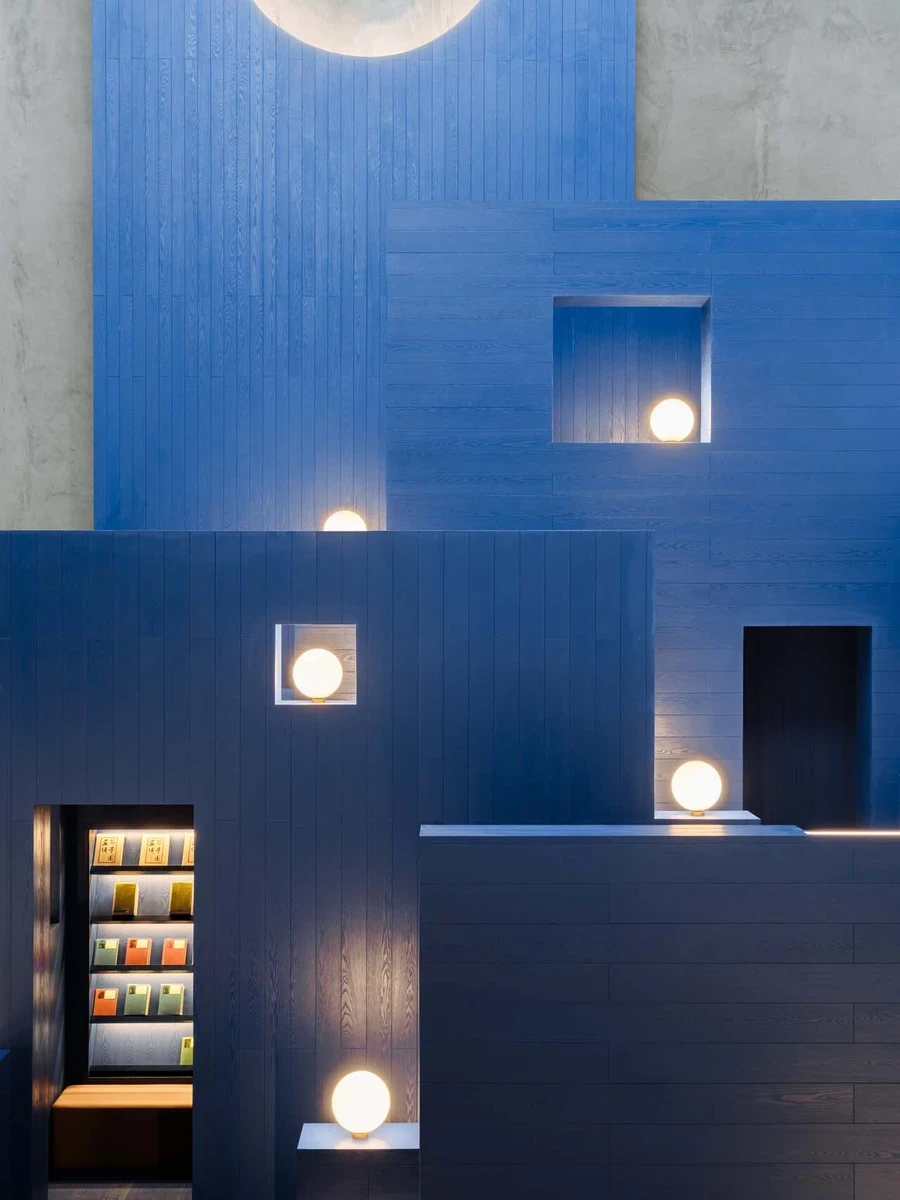 LVWA Bookstore by Studio YUDA + Studio NOR, photographed by CreatAR Images — a tight crop of the peak: stepped blue-oak terraces studded with recessed wall-niches and globe sconces, the round summit opening reading as a low moon against gray board-formed 