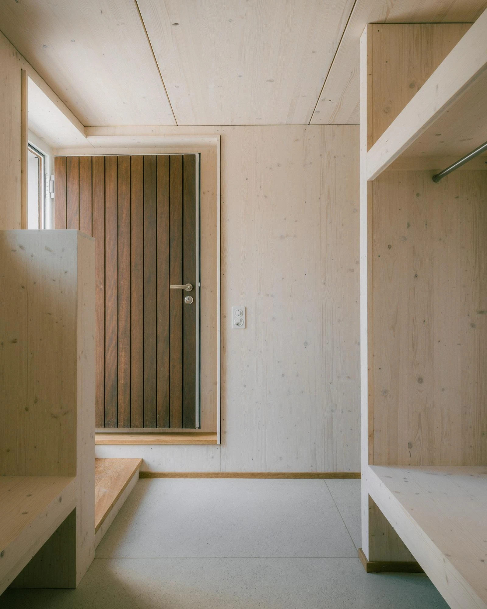 Barn Conversion in Hettlingen by Orso Dettling, photographed by Jeremiah Schwery — Entrance lobby lined in spruce CLT, a panelled dark-timber door set into a bench-and-cloakroom niche with a polished cement floor