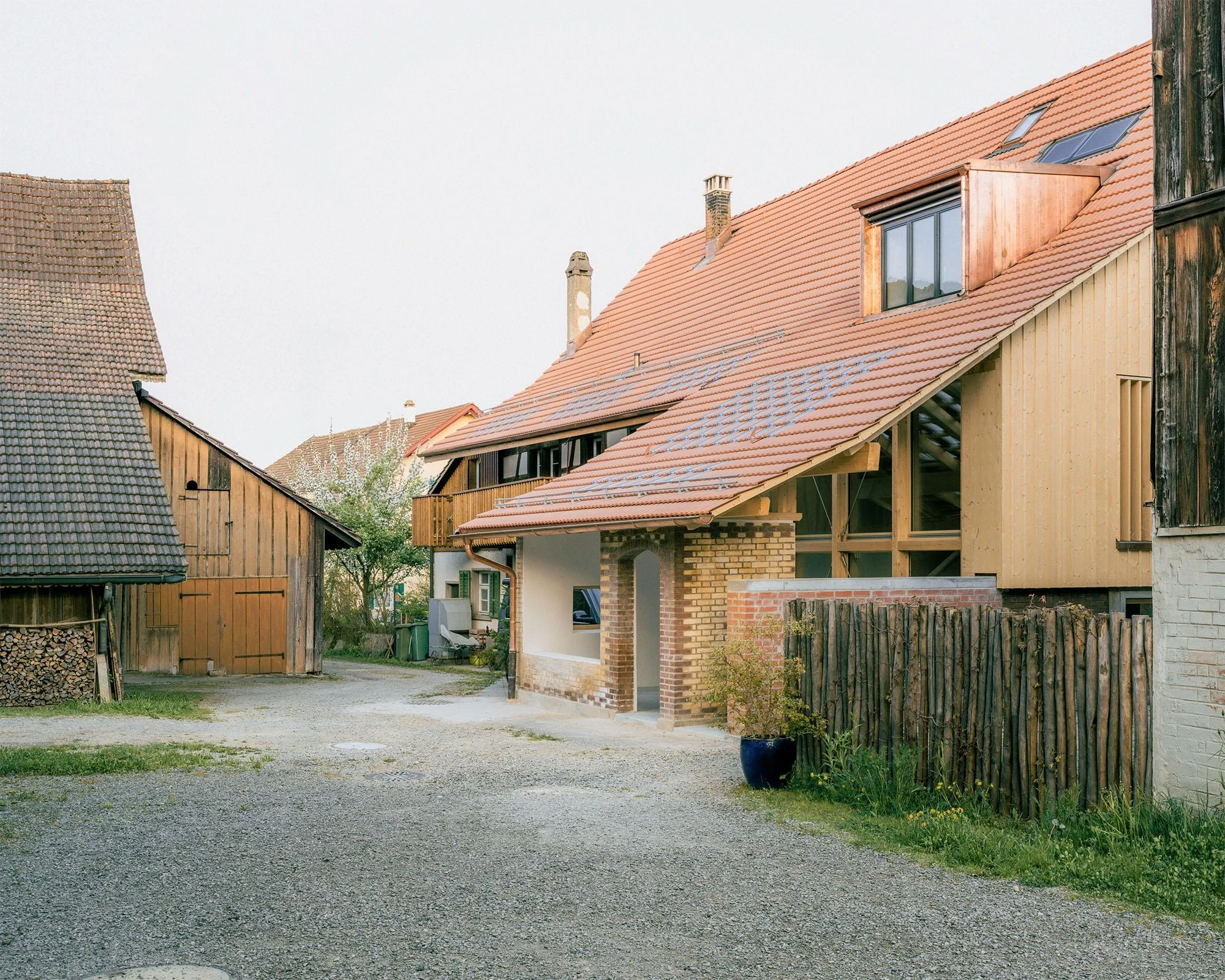 Barn Conversion in Hettlingen by Orso Dettling, photographed by Jeremiah Schwery — Forecourt view with the dormer-pierced tile roof, brick base and timber upper level set against the adjacent farm building