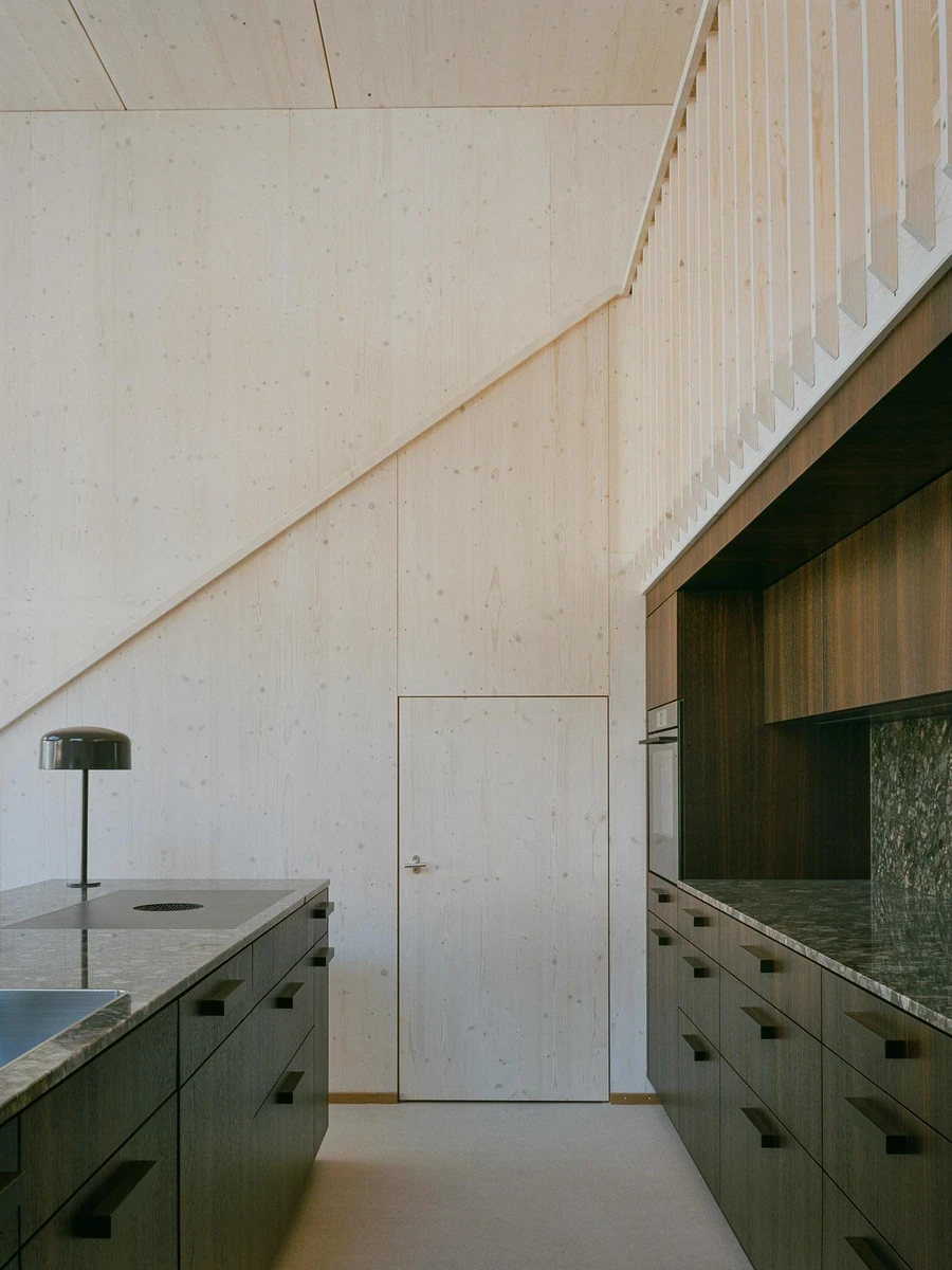 Barn Conversion in Hettlingen by Orso Dettling, photographed by Jeremiah Schwery — Kitchen seen from below the gallery, three domed table lamps lining the granite island against pale spruce panels