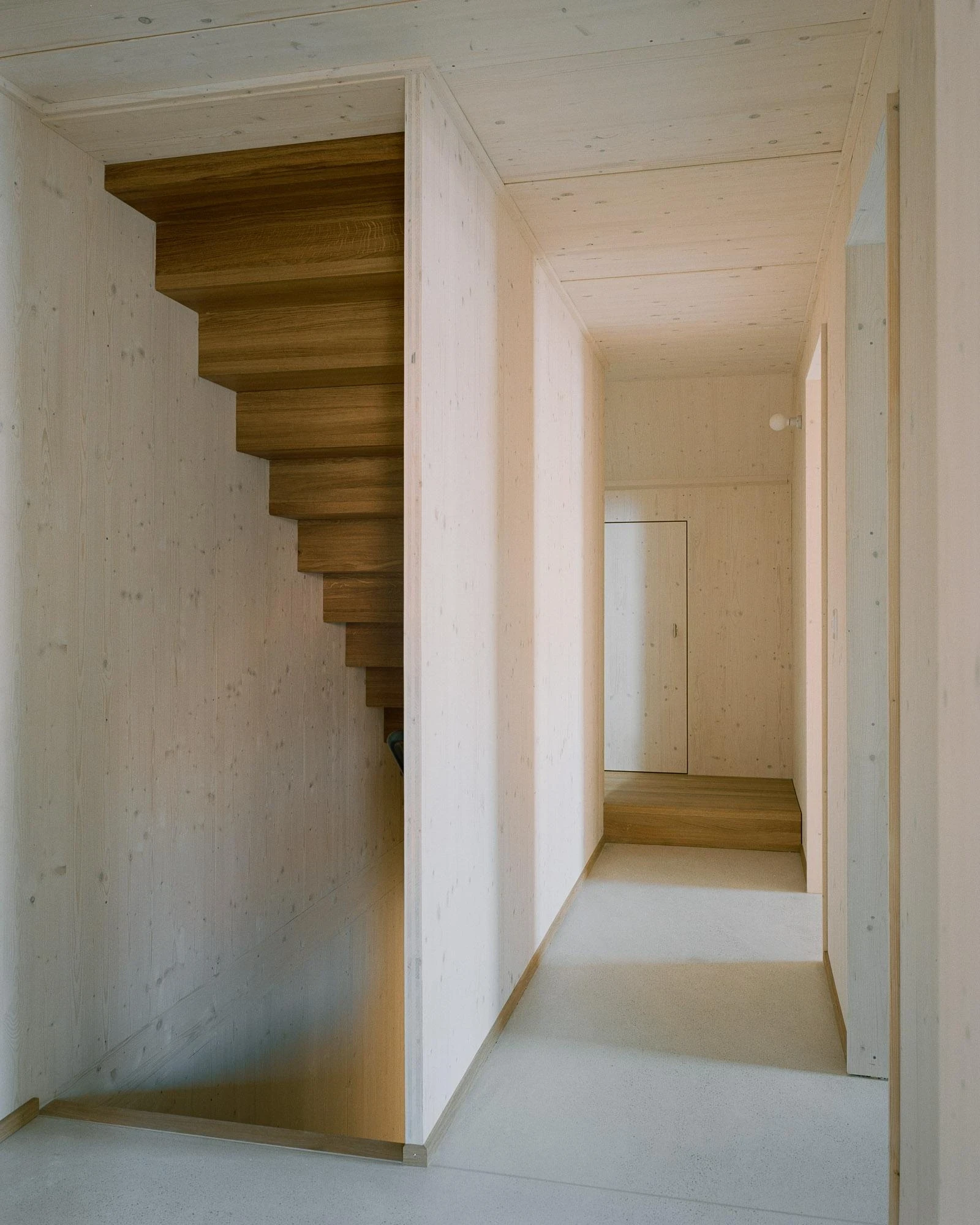 Barn Conversion in Hettlingen by Orso Dettling, photographed by Jeremiah Schwery — Hanging oak stair pulled clear of the wall, climbing through a slot in the spruce-lined gallery ceiling toward the bedrooms above