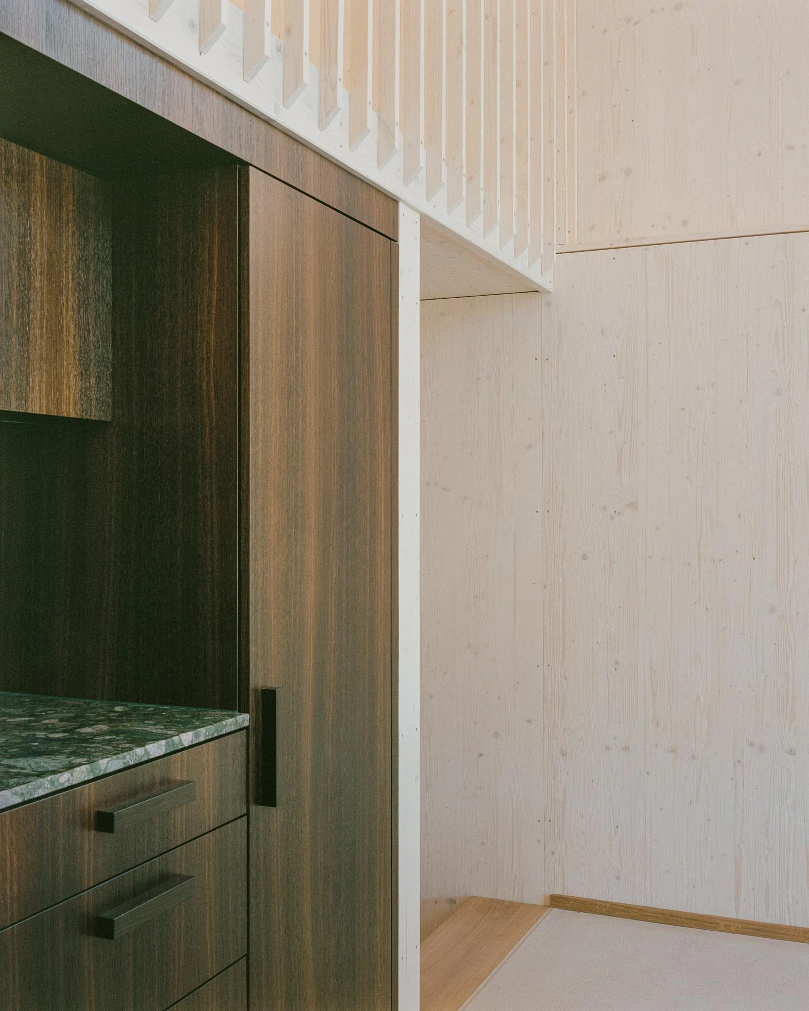 Barn Conversion in Hettlingen by Orso Dettling, photographed by Jeremiah Schwery — Kitchen island viewed against the gallery balustrade, fumed-oak cabinetry meeting pale spruce walls under a panelled ceiling