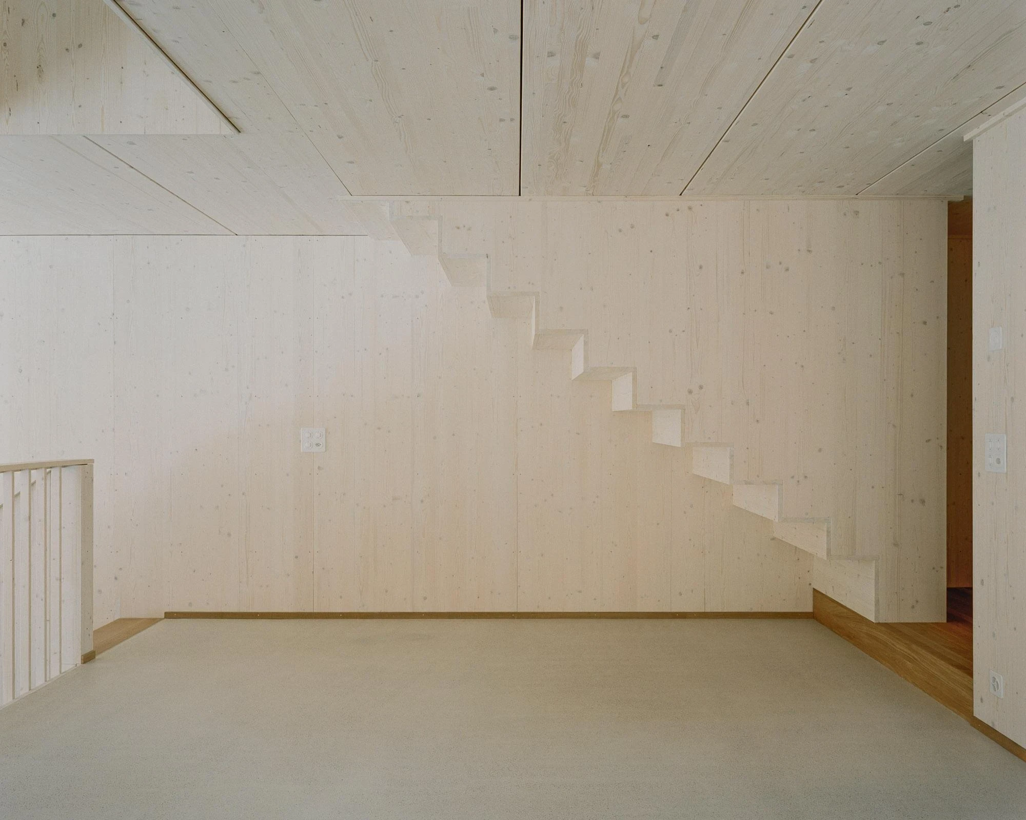 Barn Conversion in Hettlingen by Orso Dettling, photographed by Jeremiah Schwery — Gallery looking back over the kitchen, the open spruce stair folding down beside the dark island below the high panelled ceiling